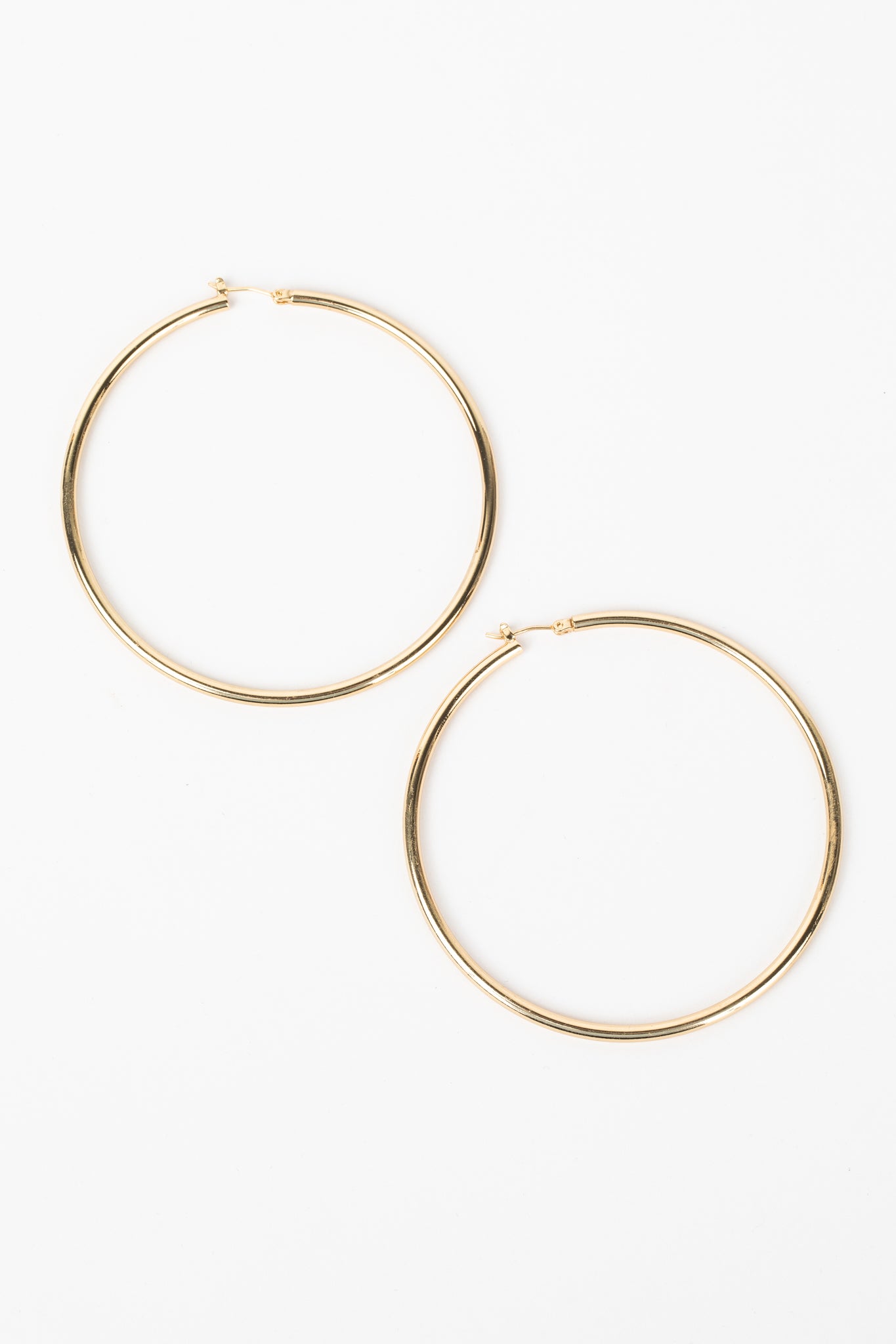 Denise Hoop Earrings 2.5 Diameter feature thin, gold-plated hoops with a sleek, rounded profile and a hinged post clasp, perfect for everyday wear.