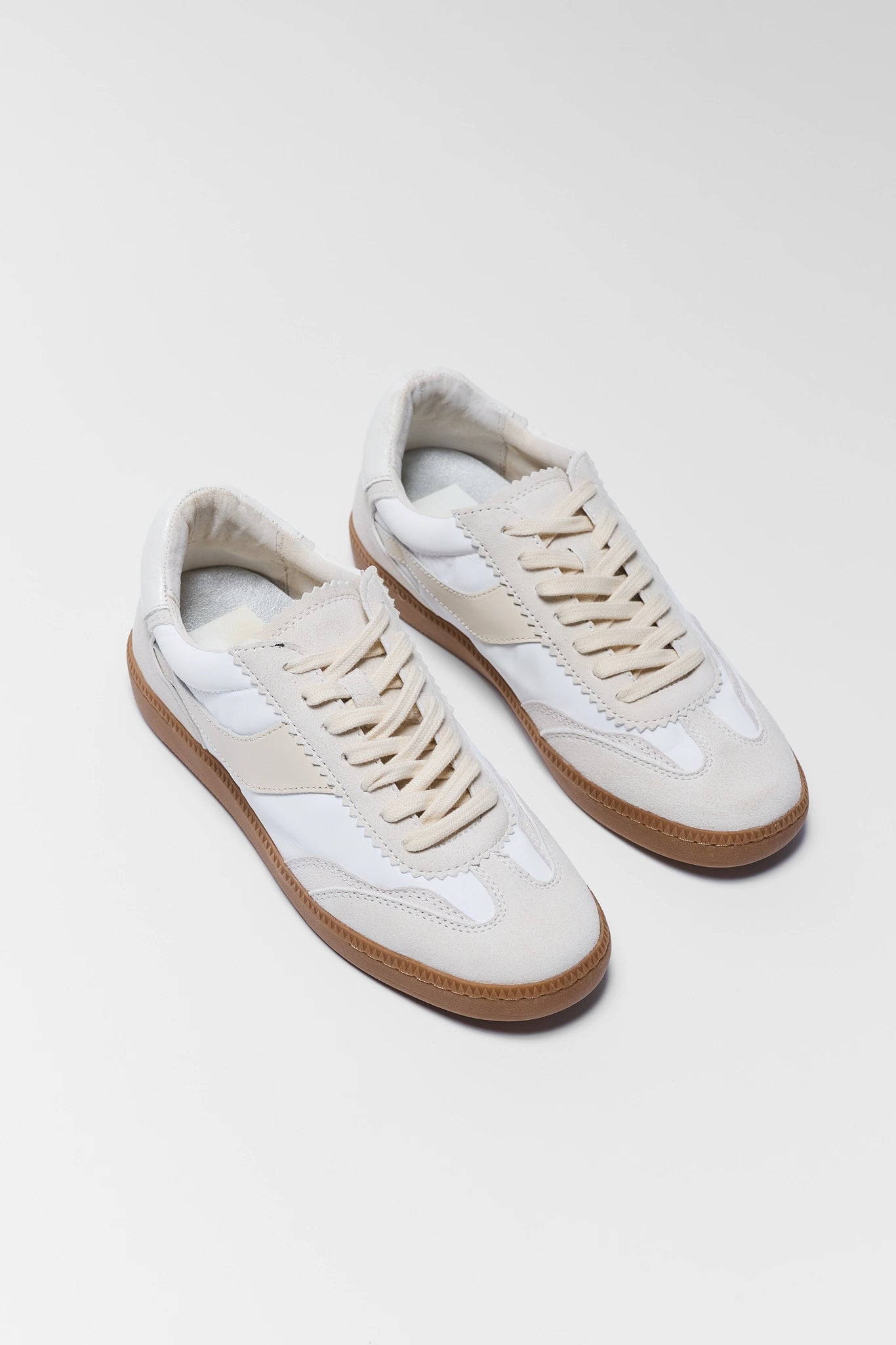 Pair of white sneakers with brown soles on a light gray background