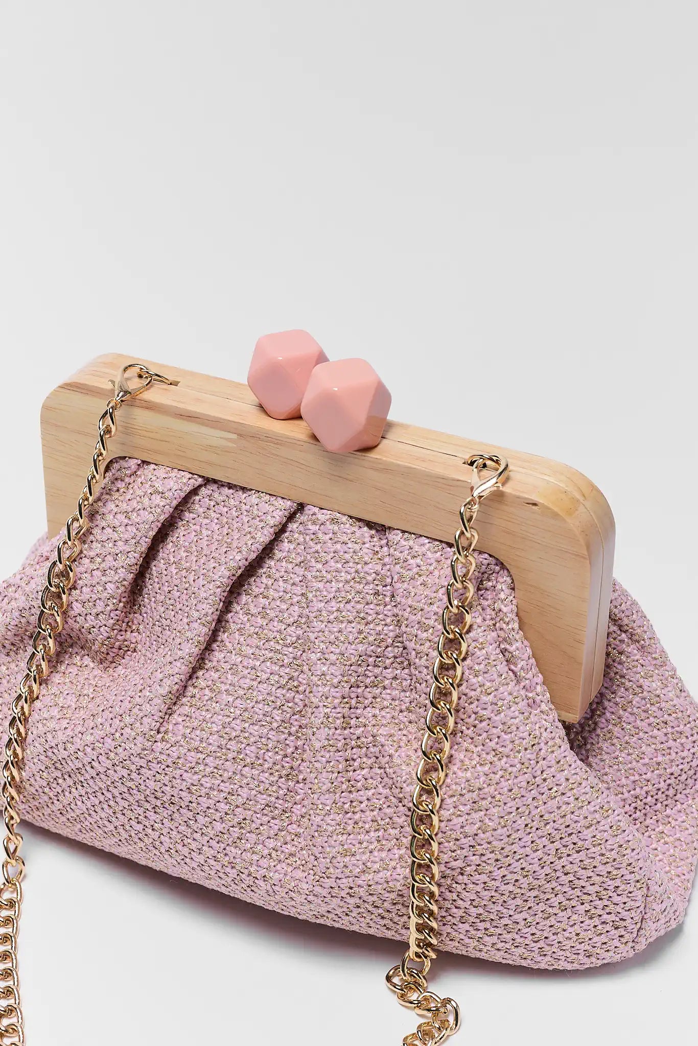 Pink textured handbag with wooden frame and gold chain strap on a light gray background
