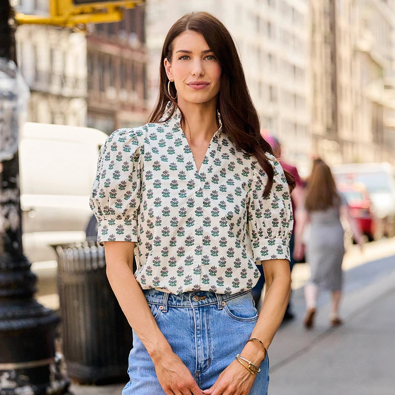 Woman wearing white block print top standing on city street corner