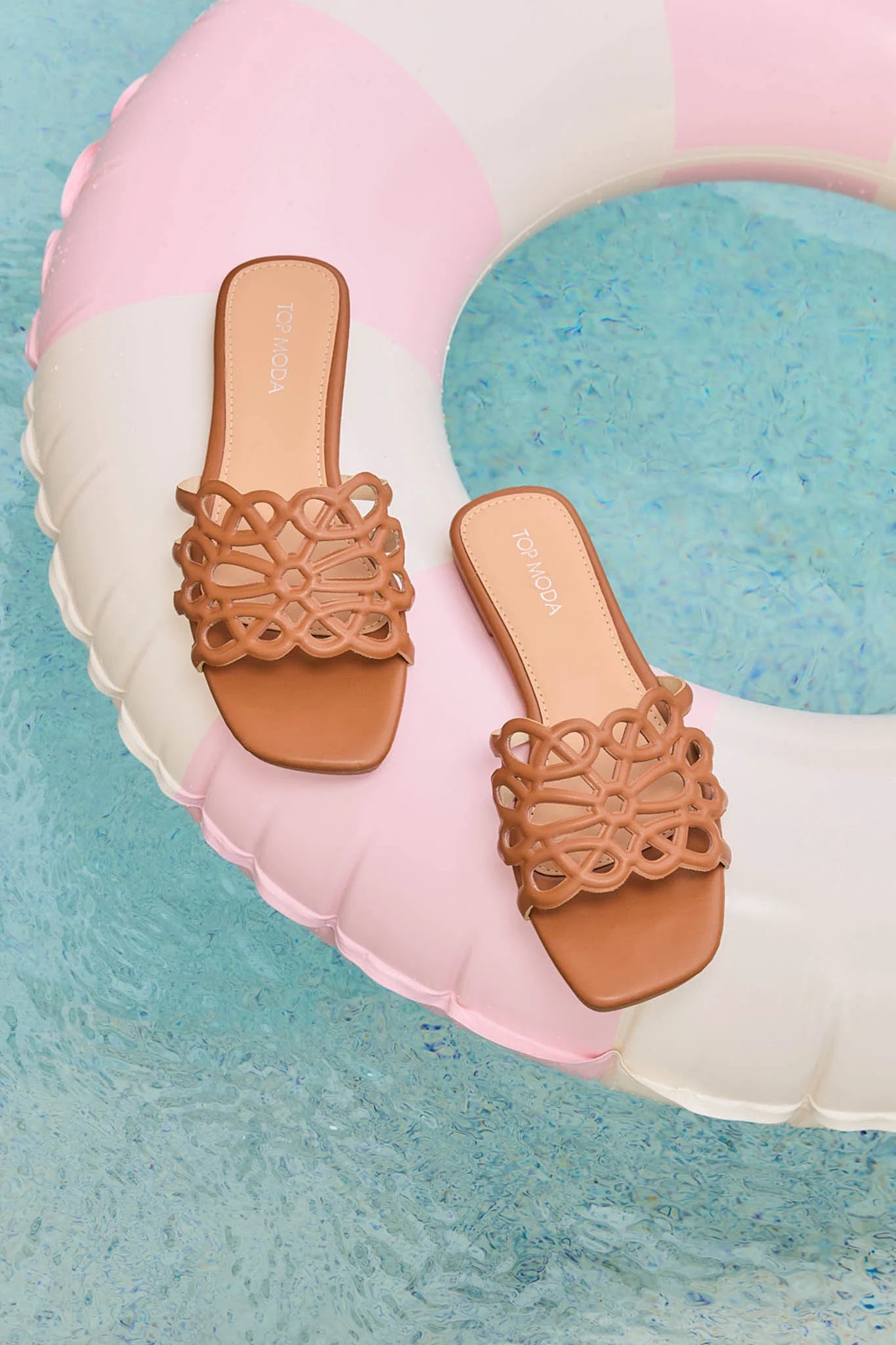 Pair of tan sandals on a colorful inflatable ring with a blue water background