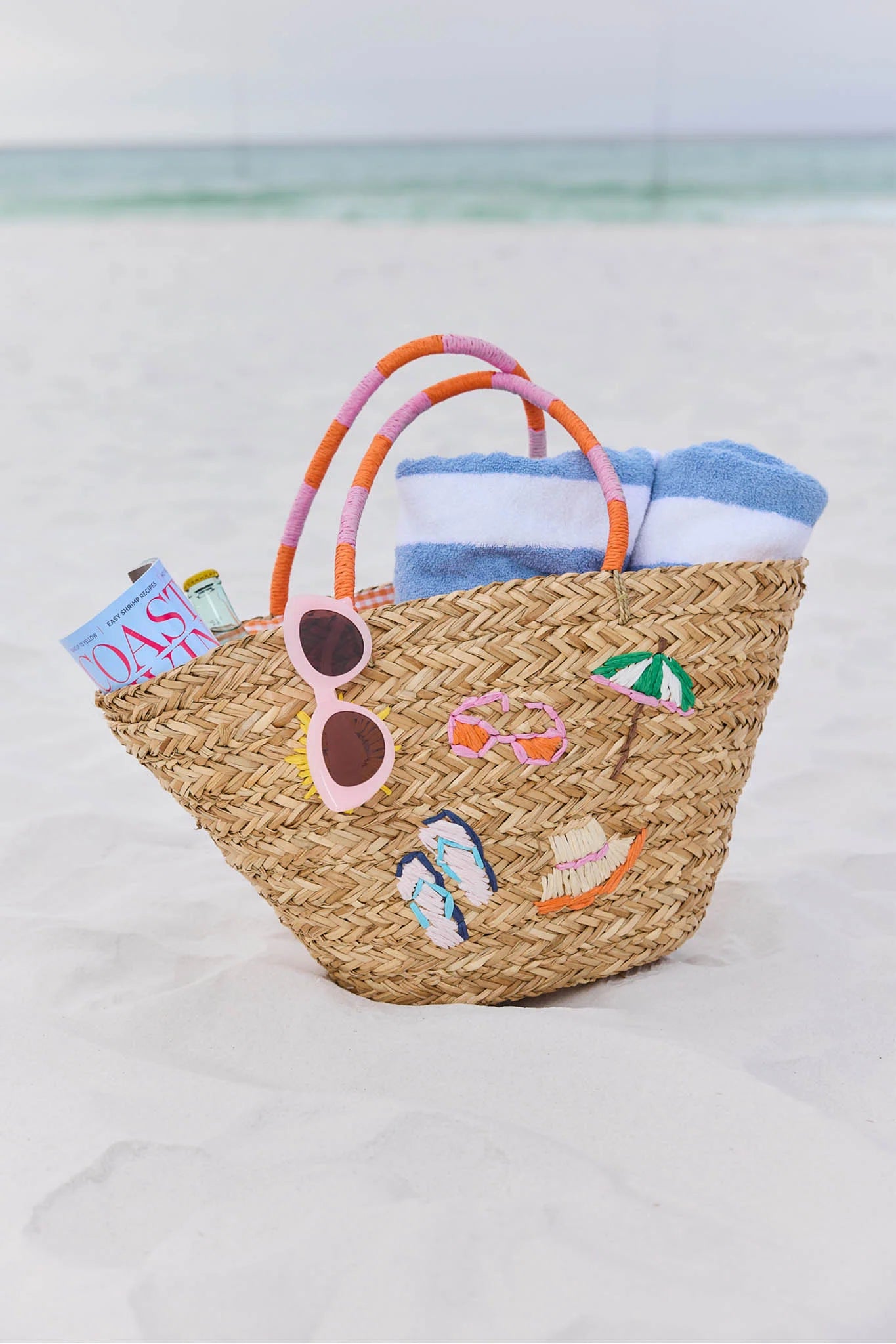 Woven beach bag with sunglasses and towels on a sandy background