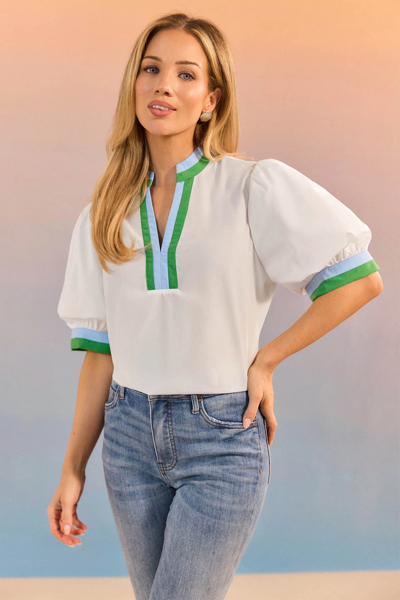 Woman wearing a white blouse with green and blue accents and blue jeans against a gradient background