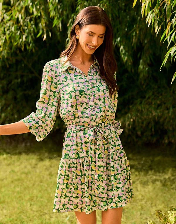 Woman wearing a green floral dress standing outdoors with greenery in the background