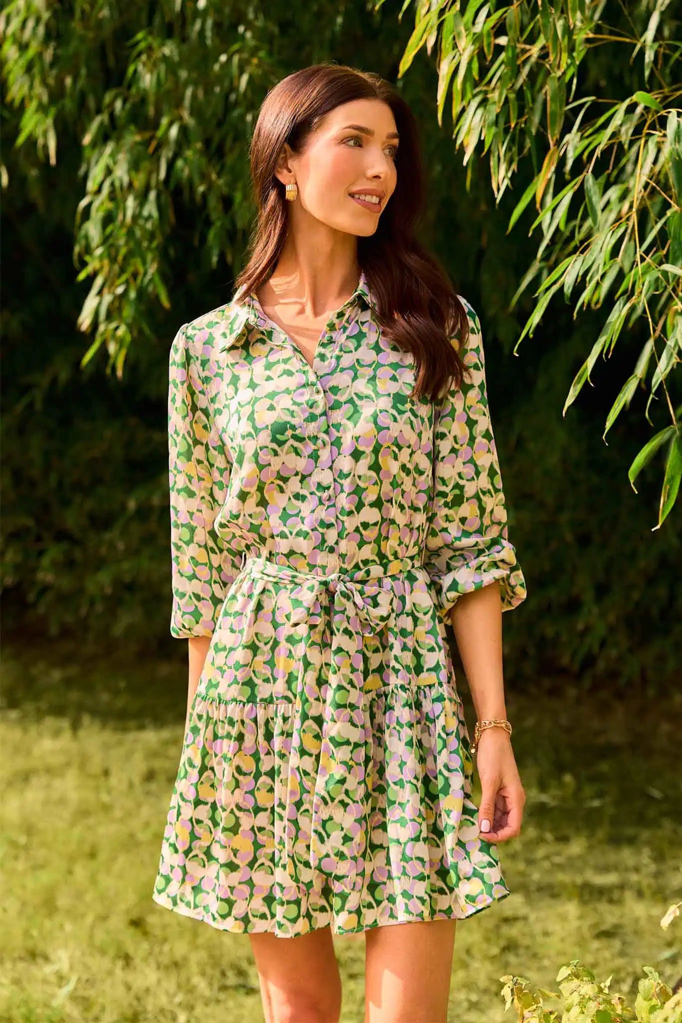 Woman wearing a green floral dress standing outdoors with greenery in the background