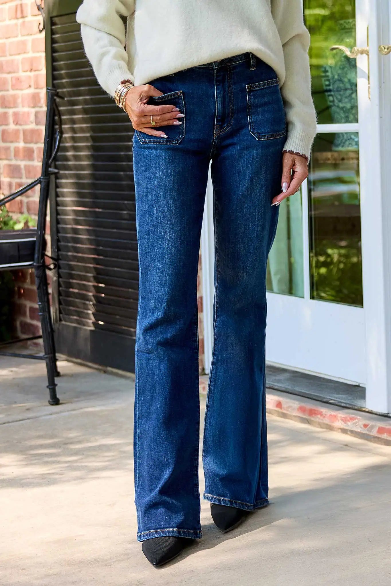 Person wearing Ana Dark Wash Flare Jeans and a light-colored sweater standing on a porch.