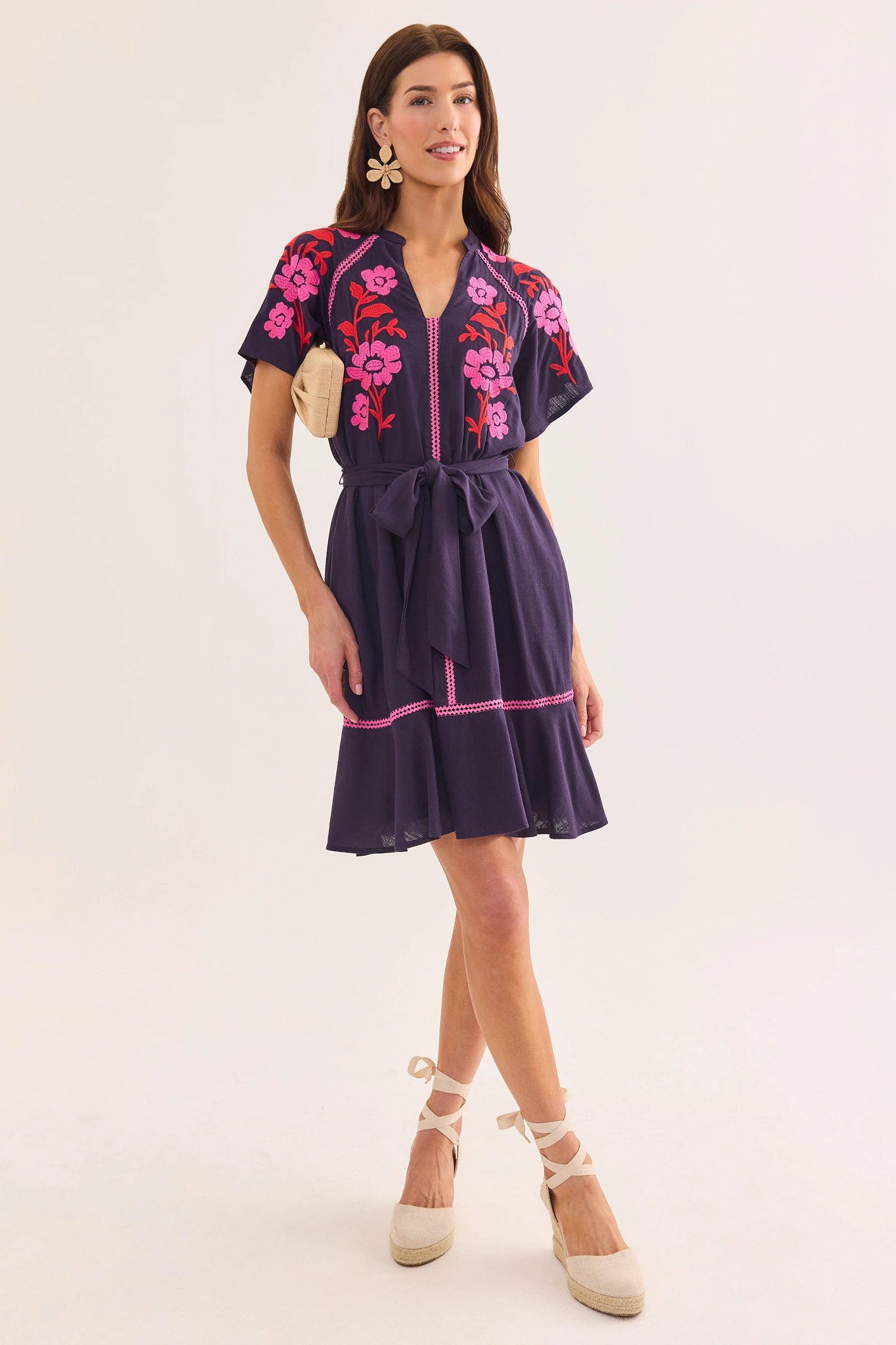 Woman wearing a navy dress with pink floral embroidery on a white background lifestyle