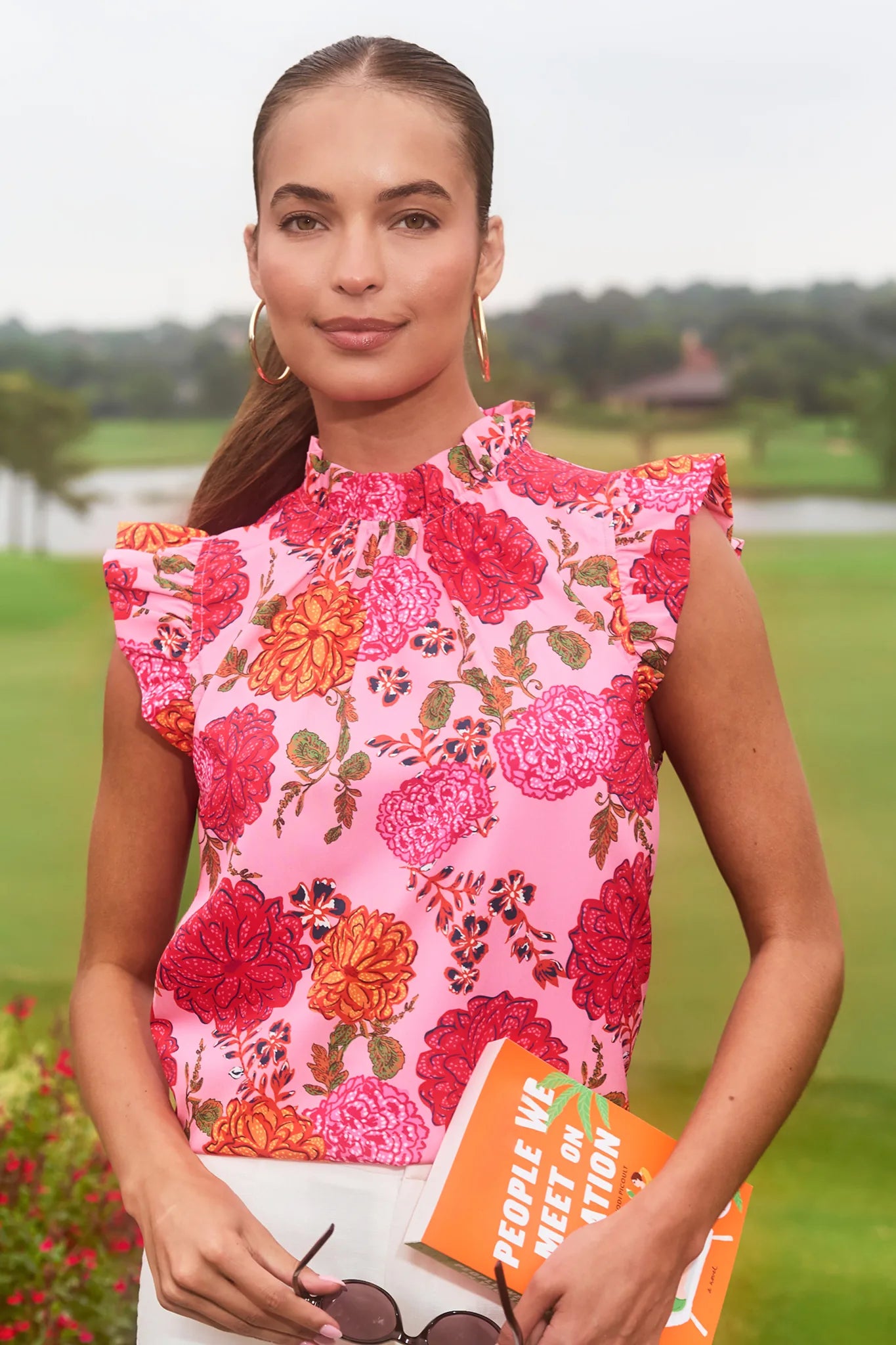 Woman wearing a pink floral dress holding a book in a park setting