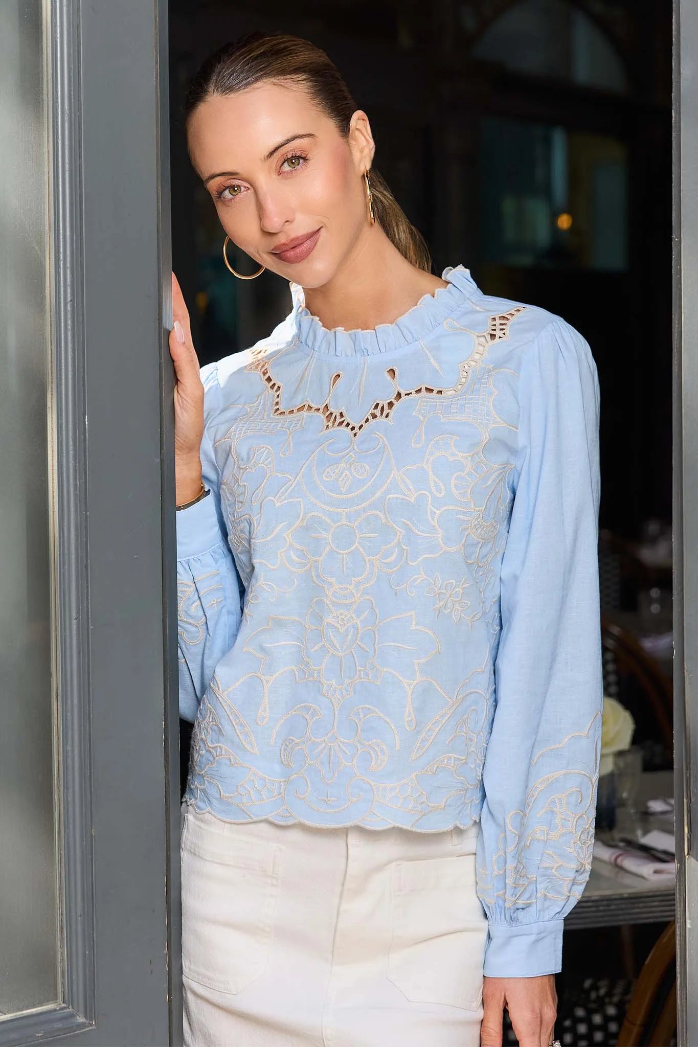 Woman wearing a light blue lace blouse standing in a doorway.