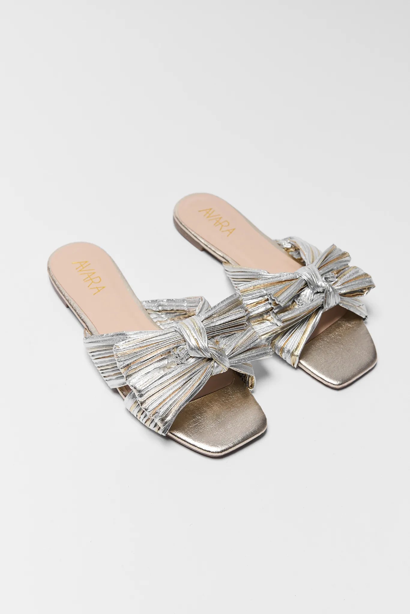 Silver and gold sandals with bow details on a white background