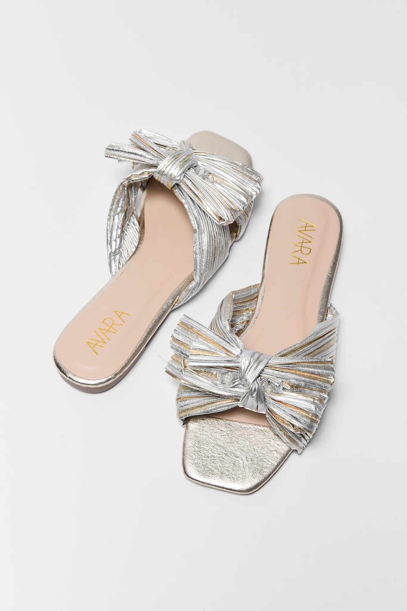 two Silver metallic sandals with bow details on a light gray background