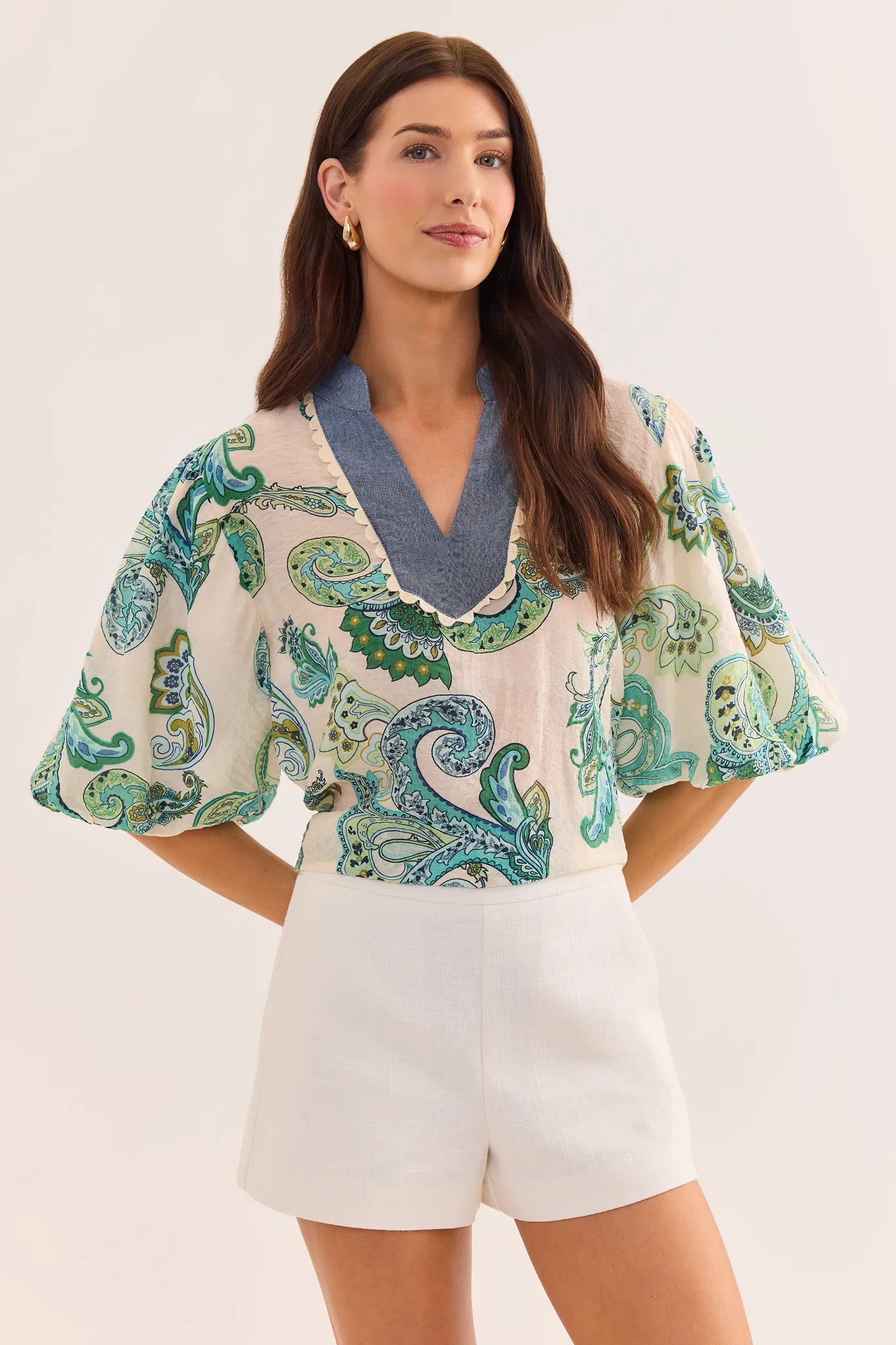 Woman wearing a patterned top and white shorts on a plain background
