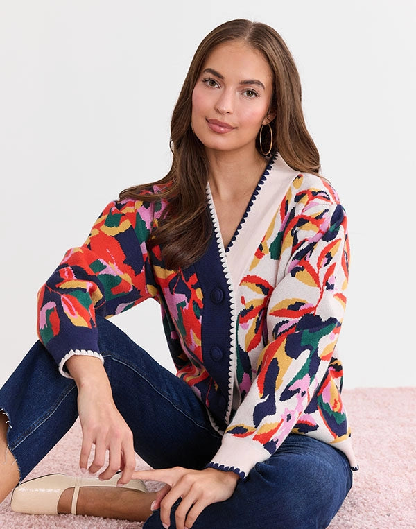 Woman wearing a colorful patterned cardigan sitting on a pink surface.