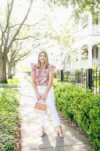 women wearing floral top and white jeans standing on sidewalk with green bushes