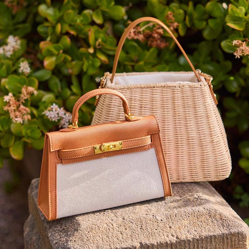Two handbags, one brown and one wicker, on a stone surface with a green foliage background.