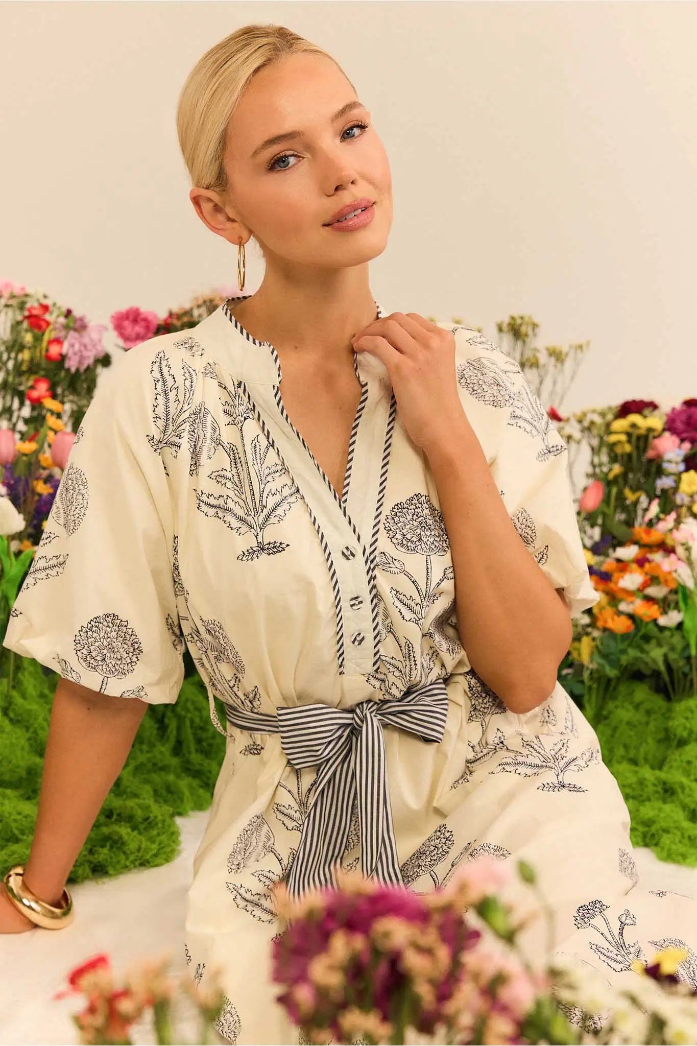 Woman in a floral dress sitting among flowers with a neutral background
