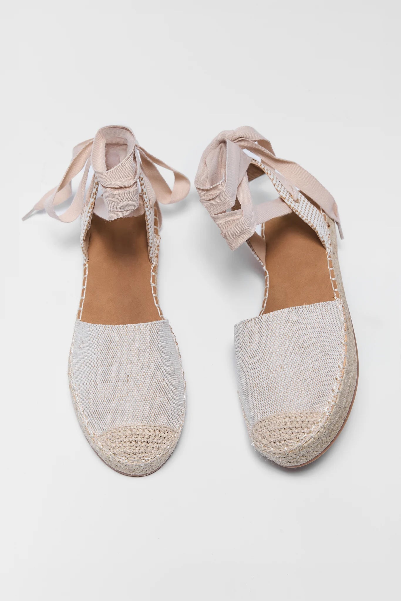 Pair of light pink espadrille shoes with woven design on a white background