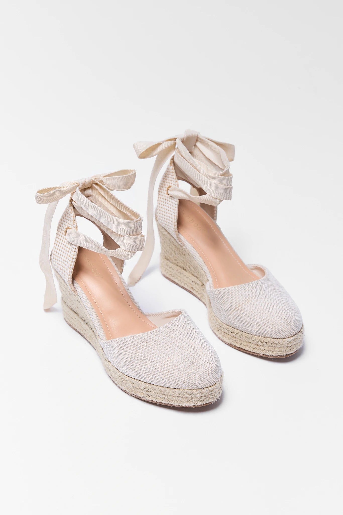 Pair of white espadrille wedge sandals with lace-up design on a light gray background