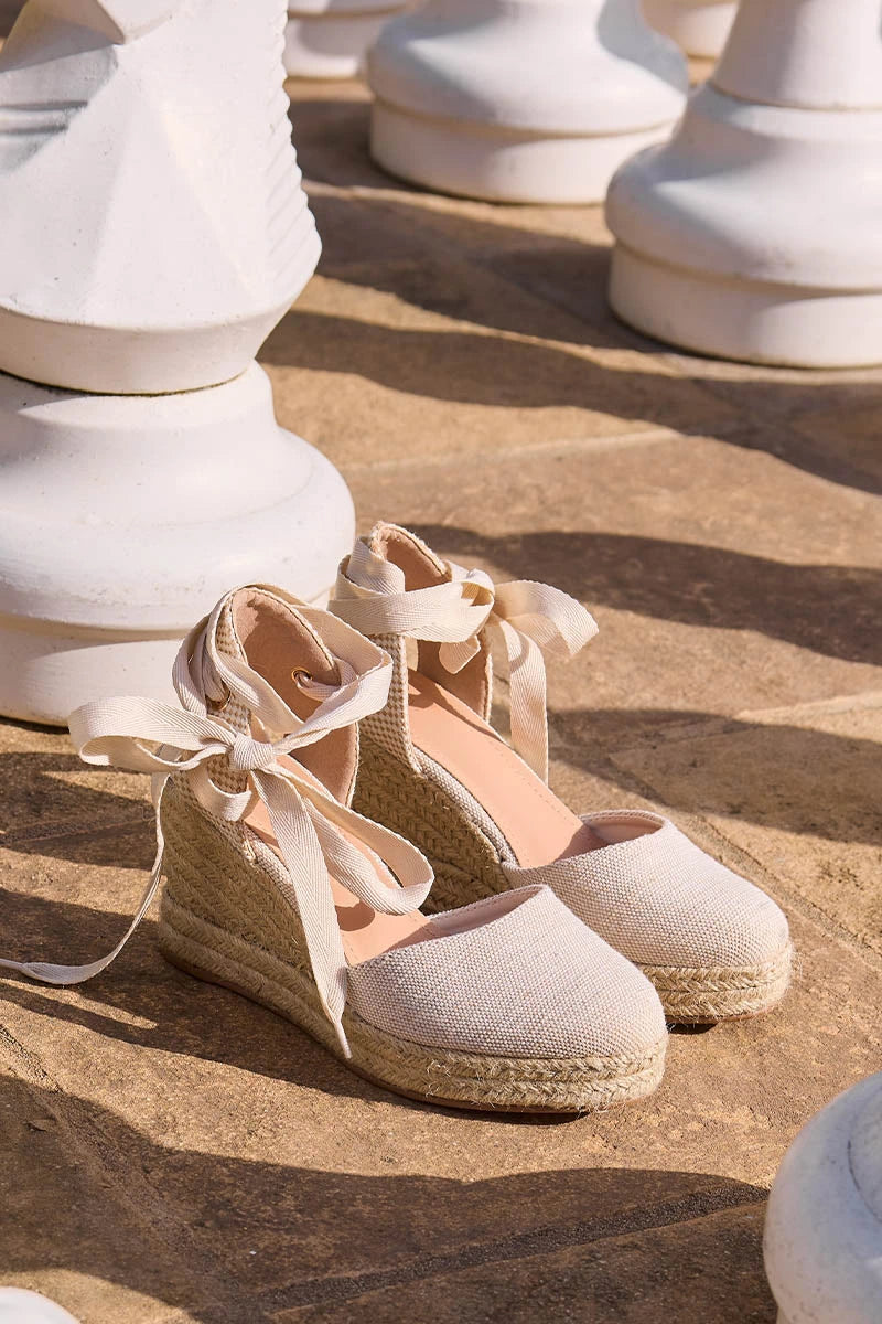 Pair of beige espadrille shoes with ribbons on a textured surface