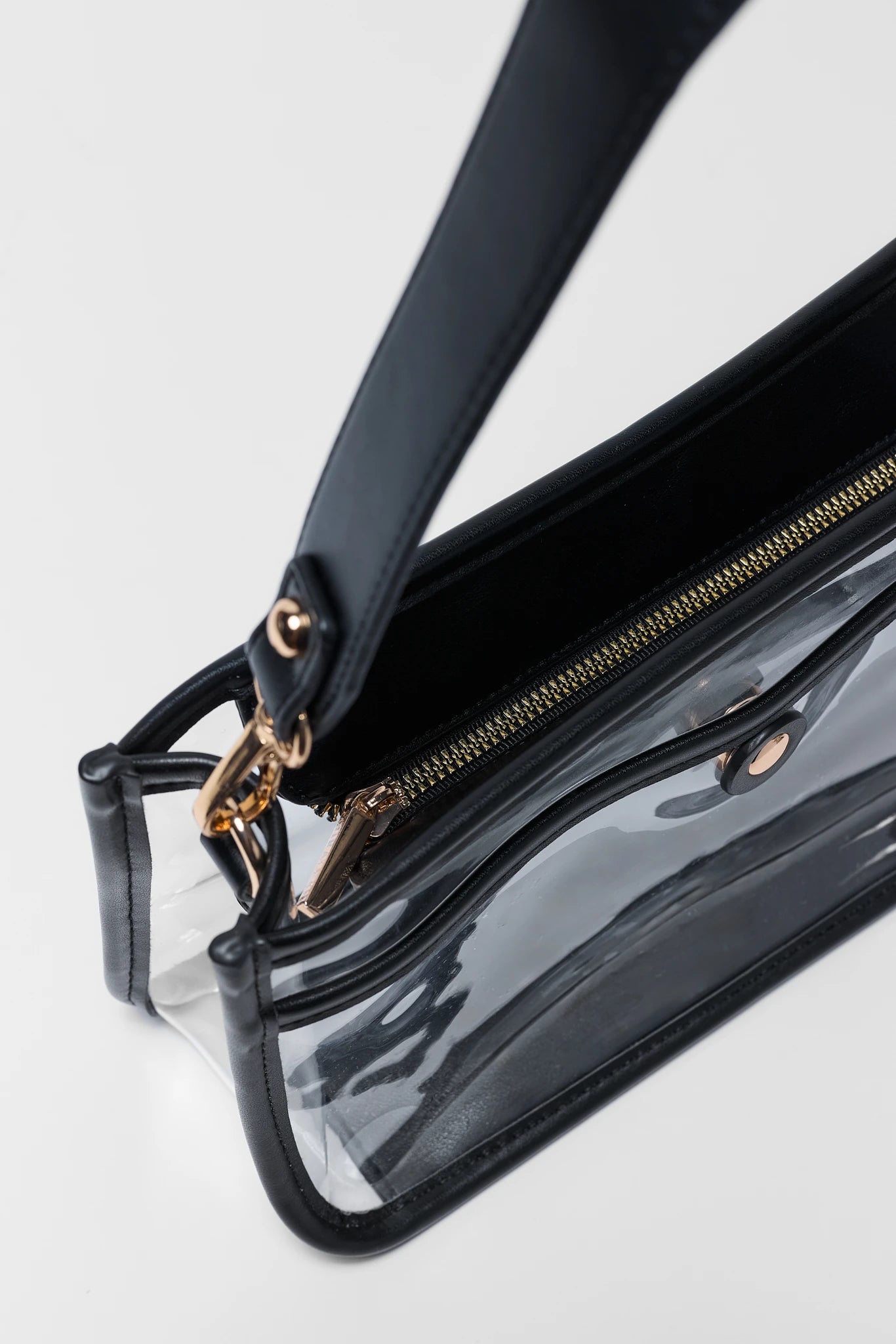 A close-up of a clear vinyl handbag with black trim, a black strap, and gold-tone hardware, including a gold zipper and ring pull.