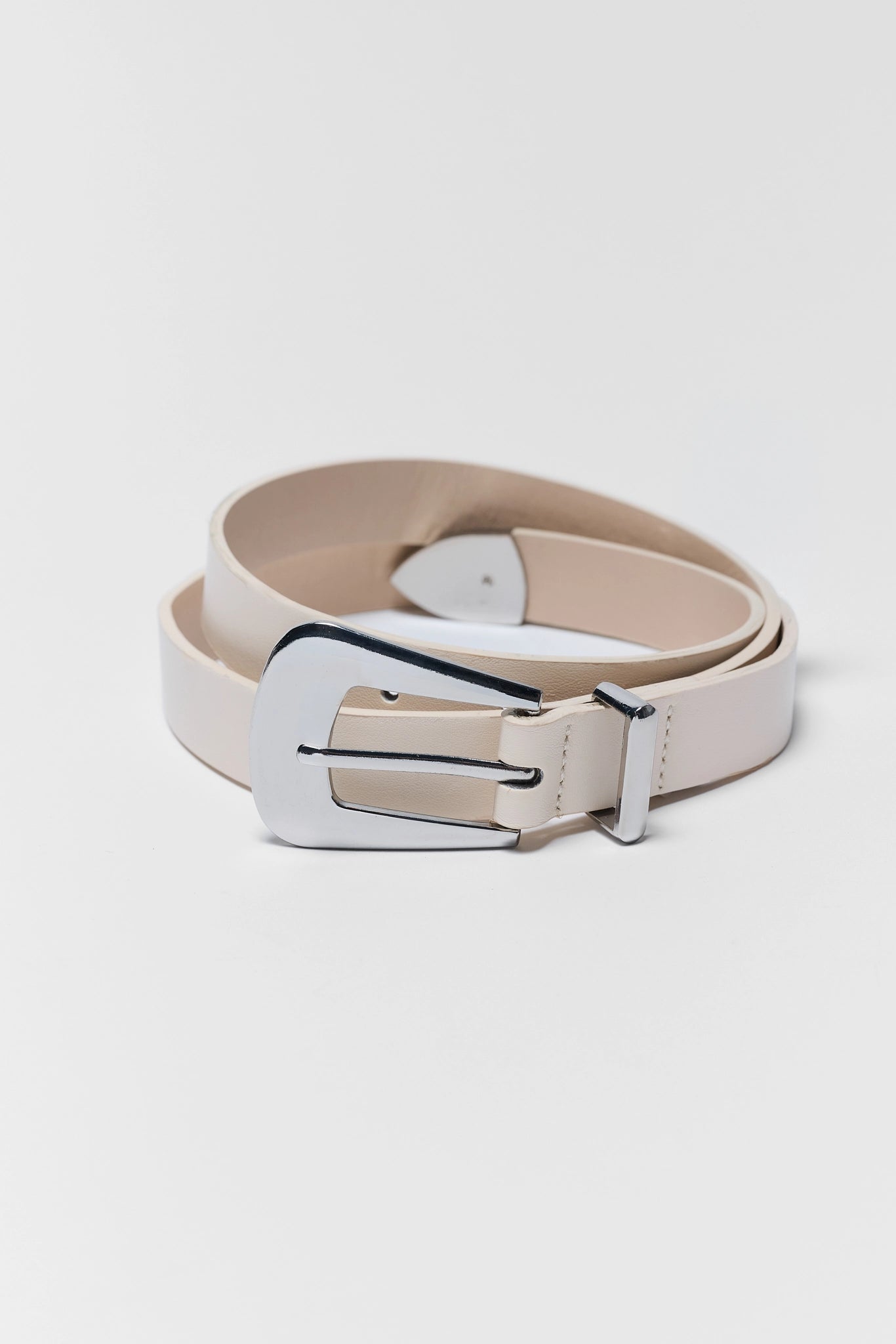 A light beige leather belt with a polished silver-tone metal buckle, coiled on a light gray background.