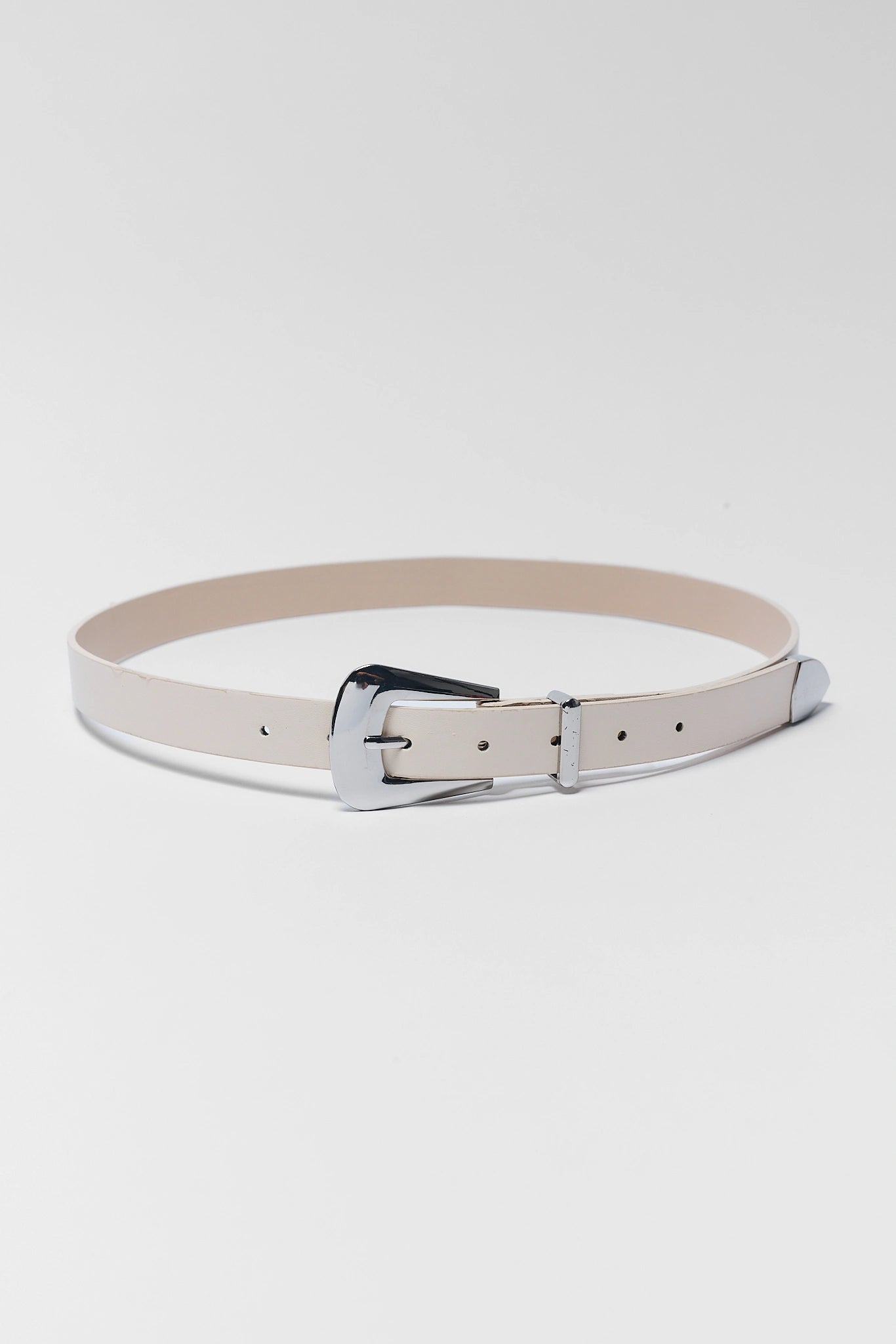 A slim, light beige leather belt with a polished silver-tone metal buckle, displayed in a coiled shape against a clean, light gray studio background.