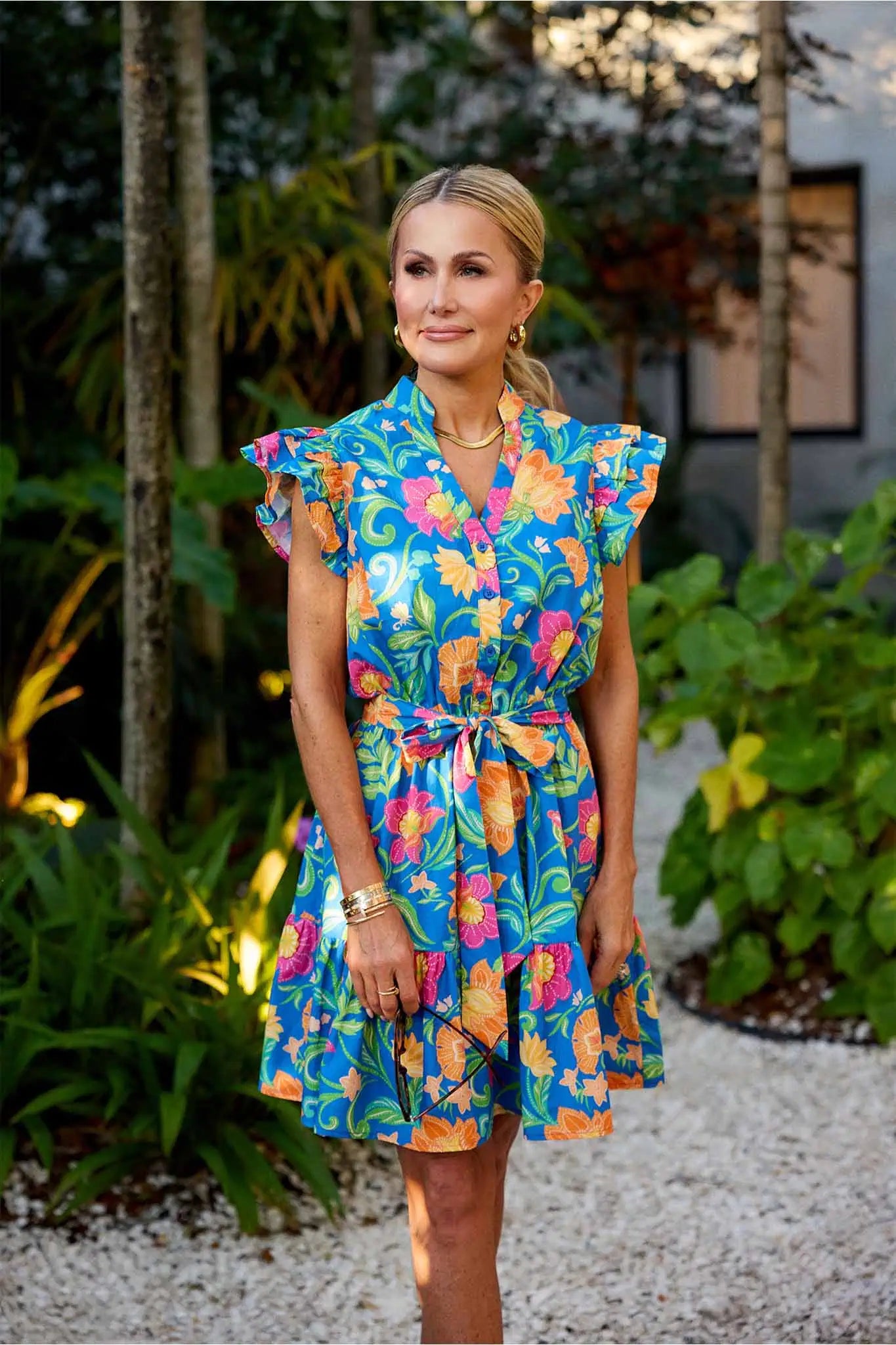 Woman wearing a colorful floral dress standing outdoors with greenery in the background