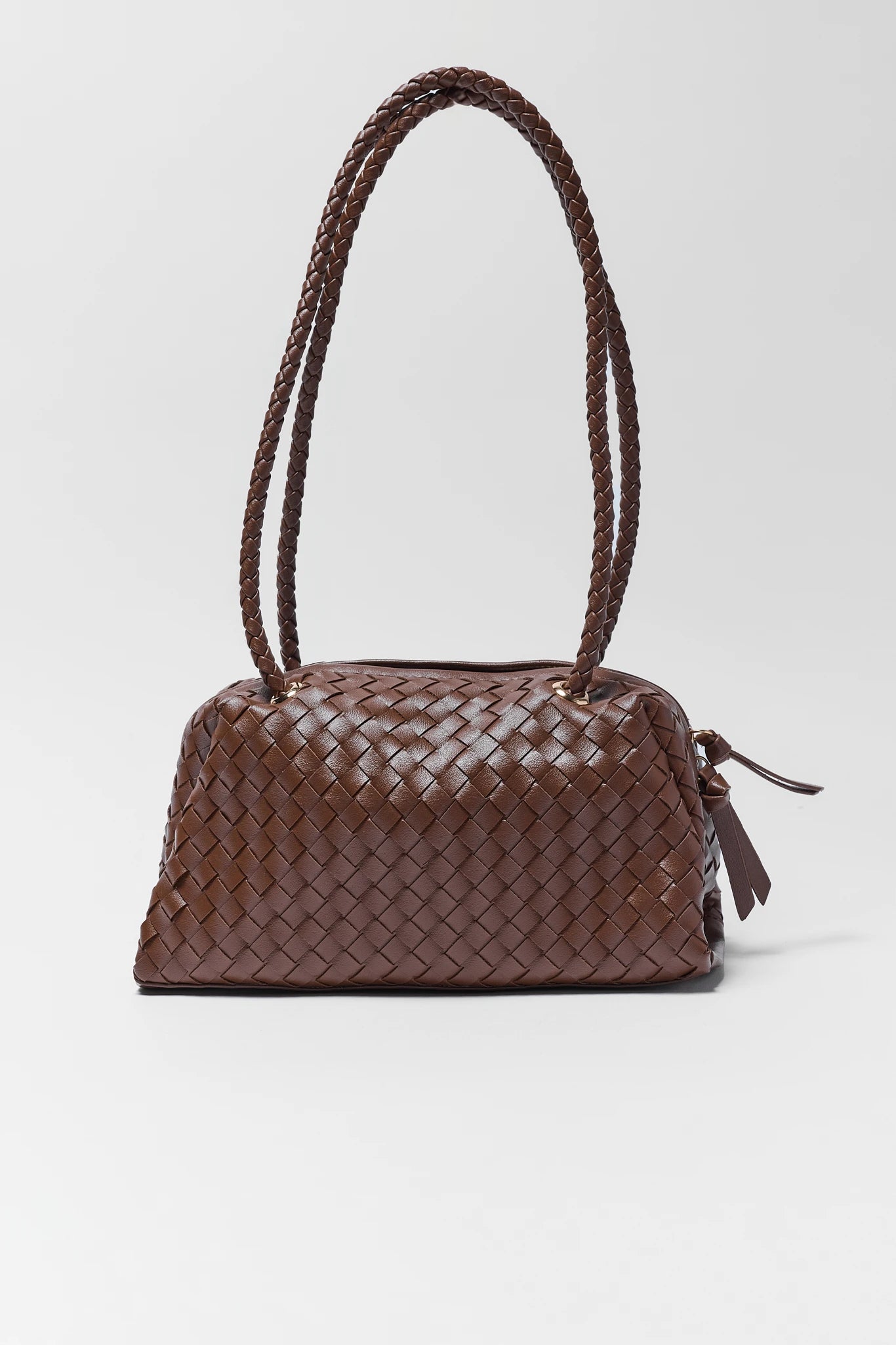 A brown woven leather handbag with a structured dome shape, dual braided shoulder straps, and a small leather tassel detail on the side, photographed against a light gray studio background.