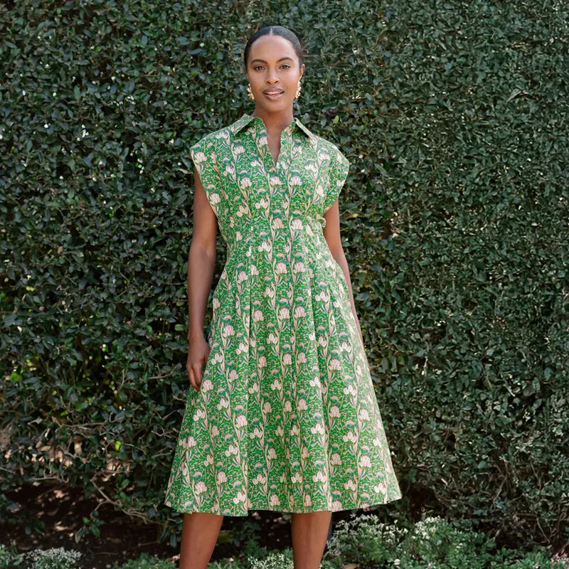 Woman wearing a green floral dress standing against a hedge.