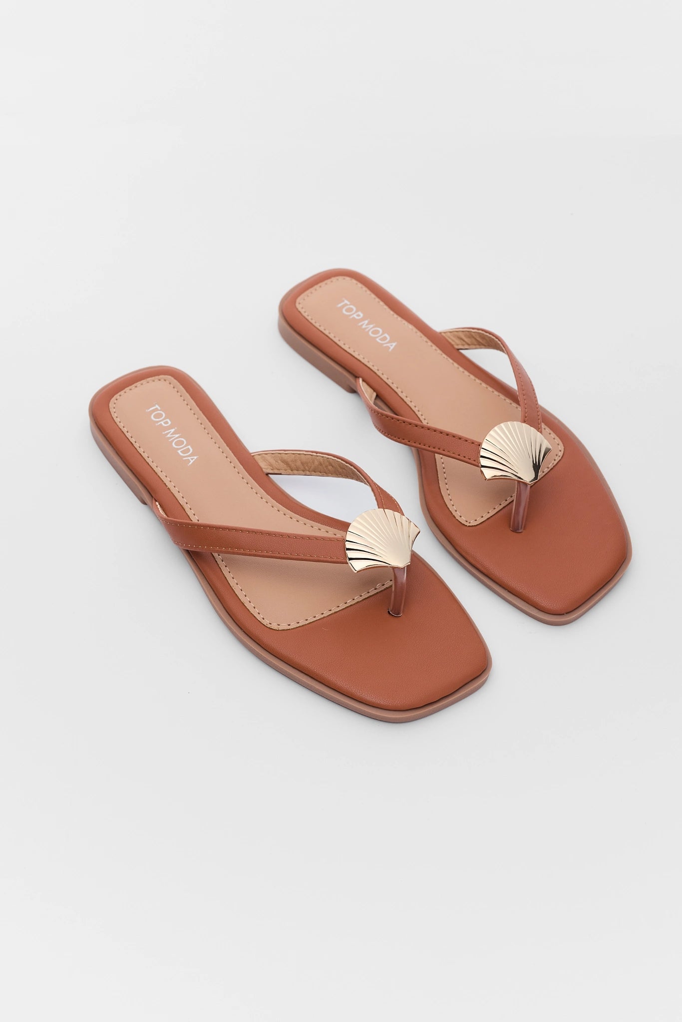 Pair of brown sandals with shell decorations on a light background