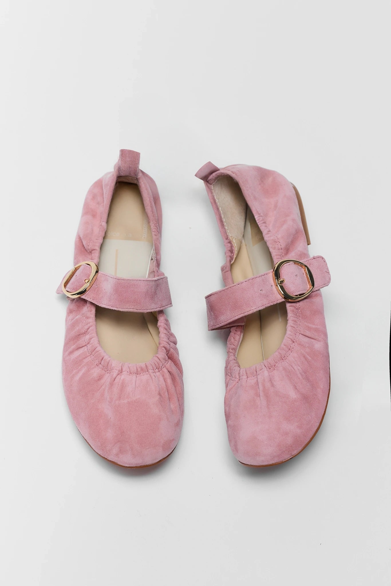 Pair of pink suede shoes with buckles on a light gray background