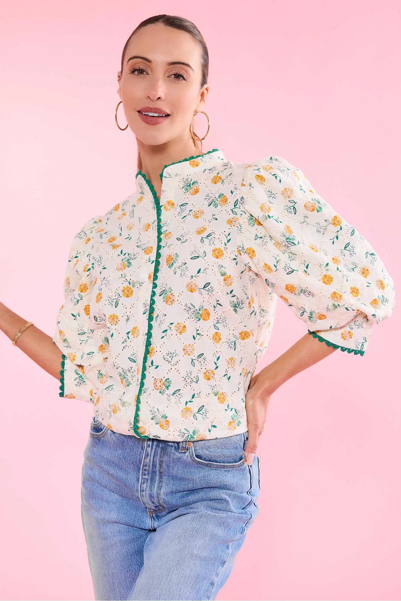 Woman wearing a floral blouse with green trim on a pink background