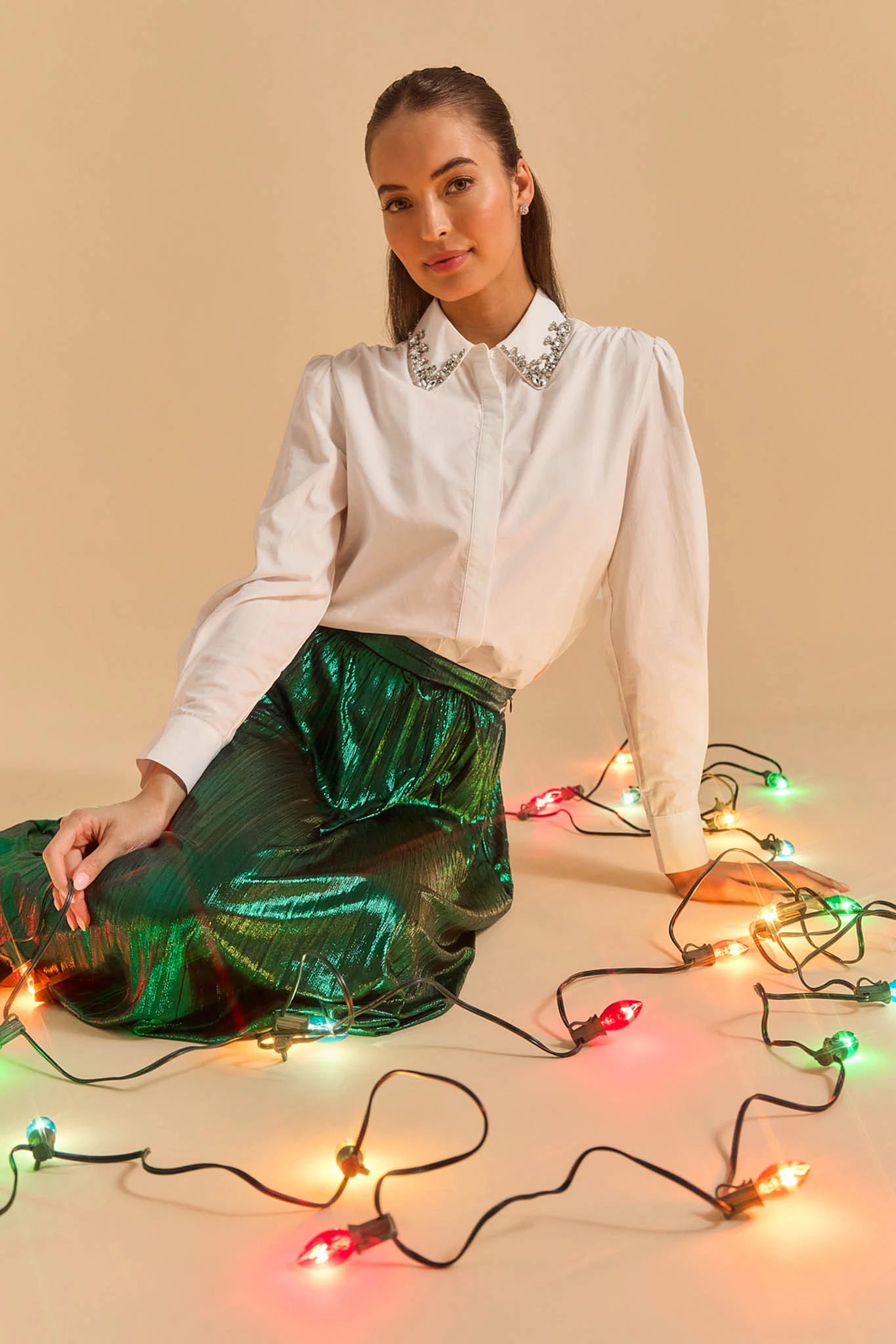 Woman in a white Celeste Top and green skirt surrounded by colorful Christmas lights on a beige background