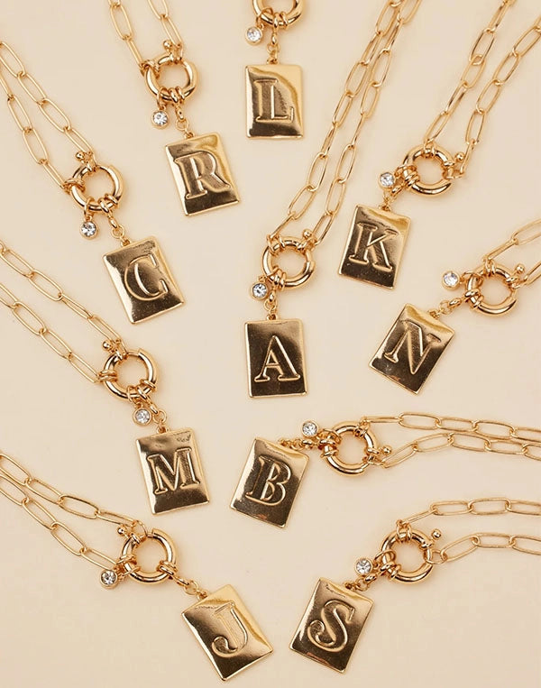 Gold necklaces with letter pendants on a beige background
