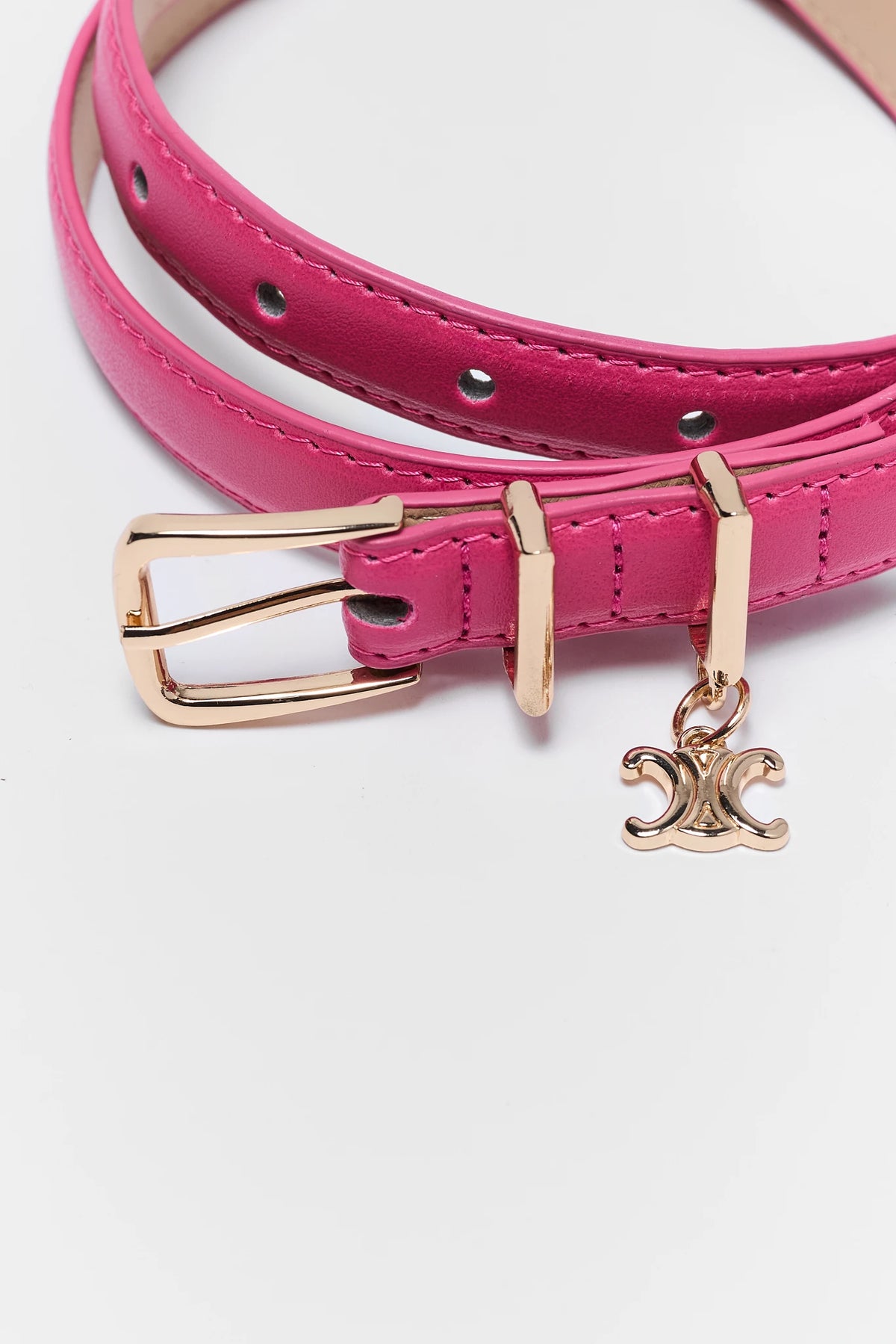 A close-up of a bright pink leather belt with a gold-tone buckle and a dangling Celine logo charm, set against a plain white background.