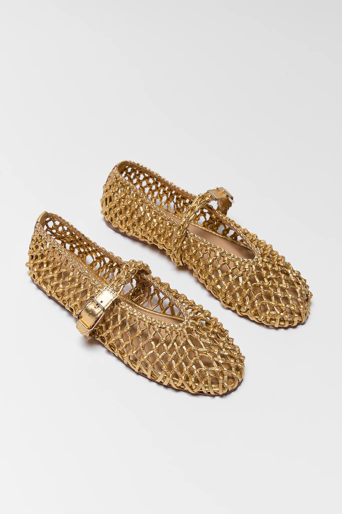 Pair of gold woven shoes on a light gray background two