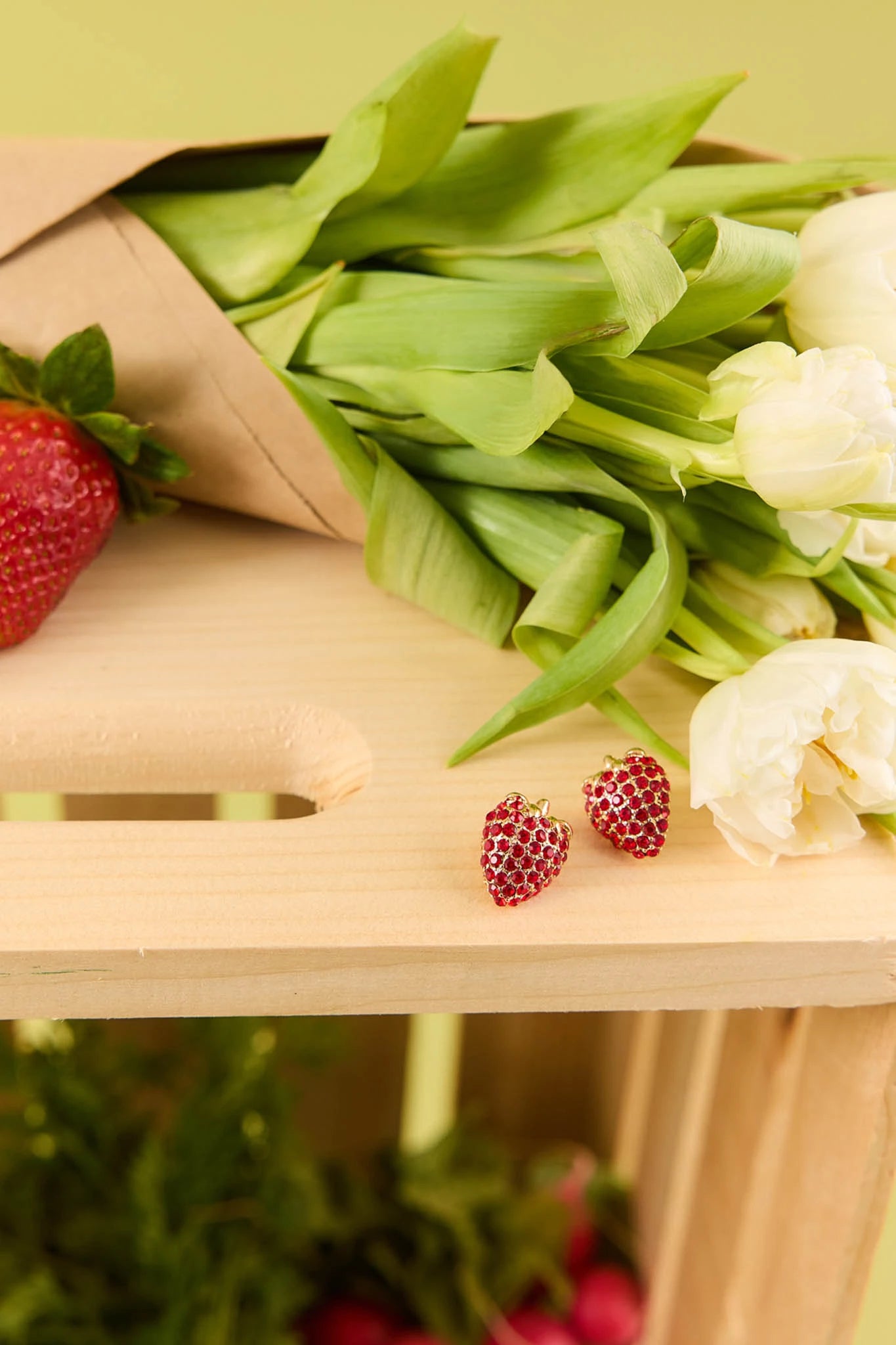 Bouquet of green onions, strawberries, and cauliflower on a wooden surface with a blurred green background.