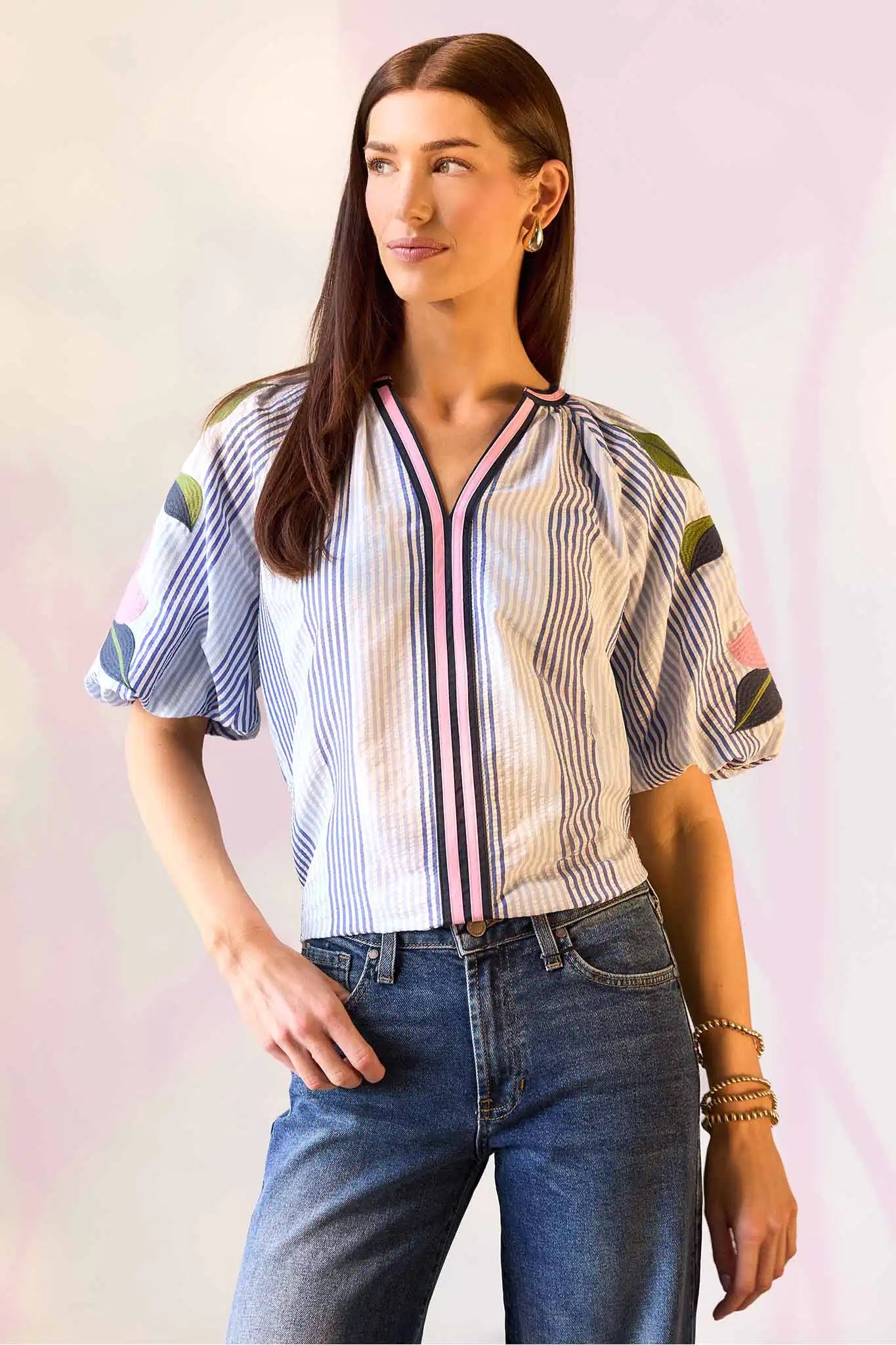 Woman wearing a colorful striped shirt and jeans on a light pink background