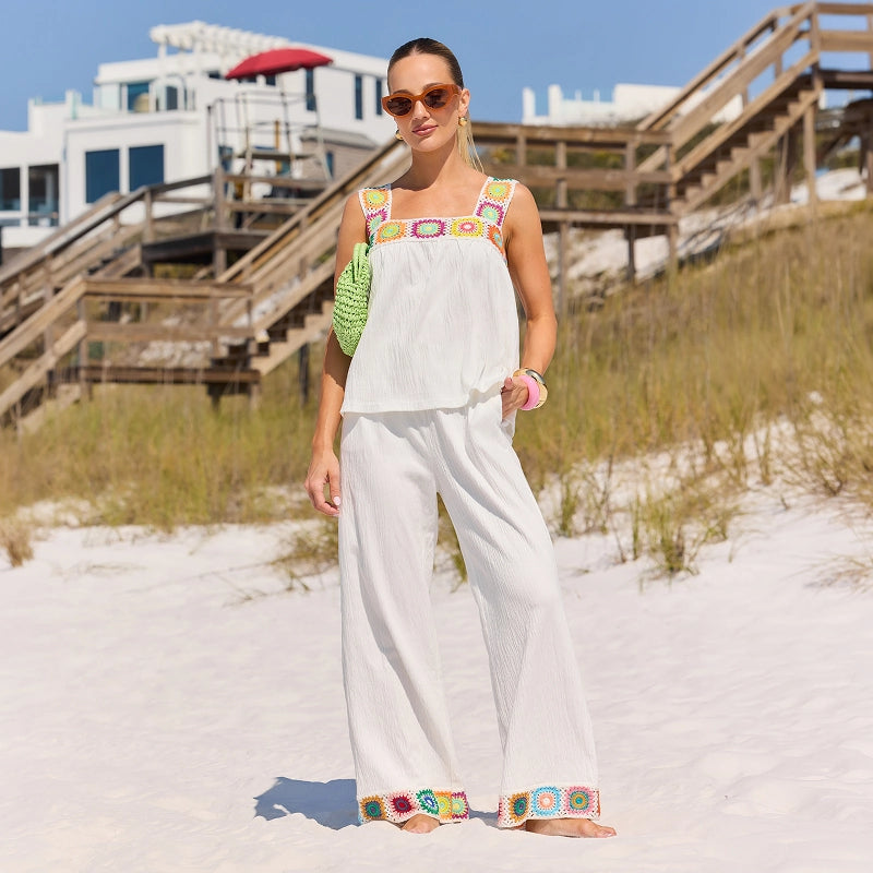 Woman in a white outfit with colorful accents standing on a sandy beach. collection