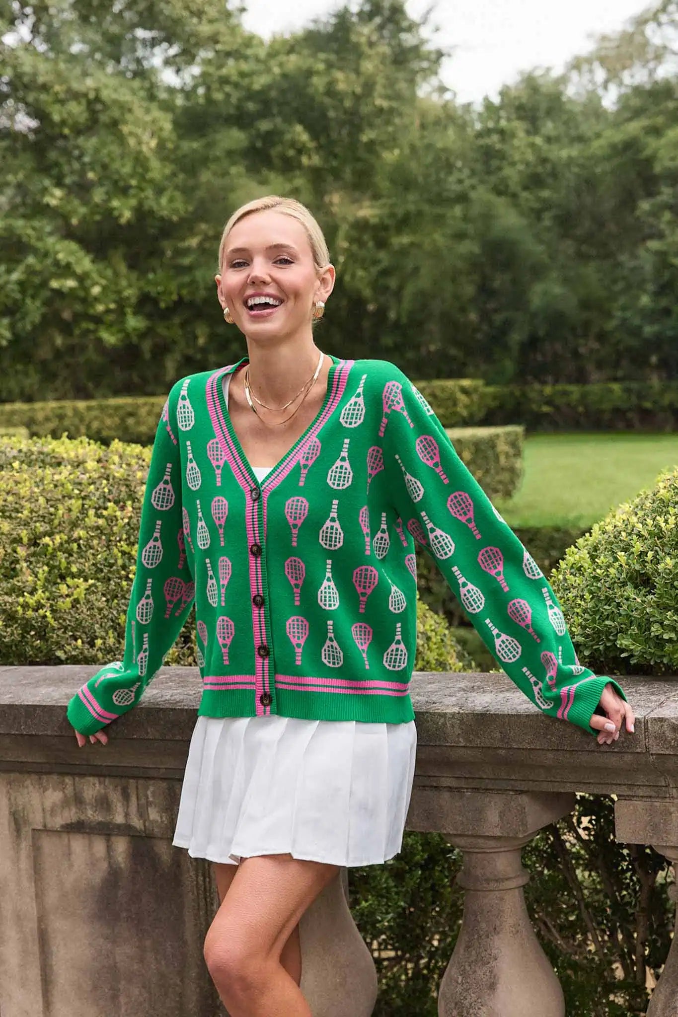 Woman wearing a green patterned cardigan and white skirt standing outdoors.