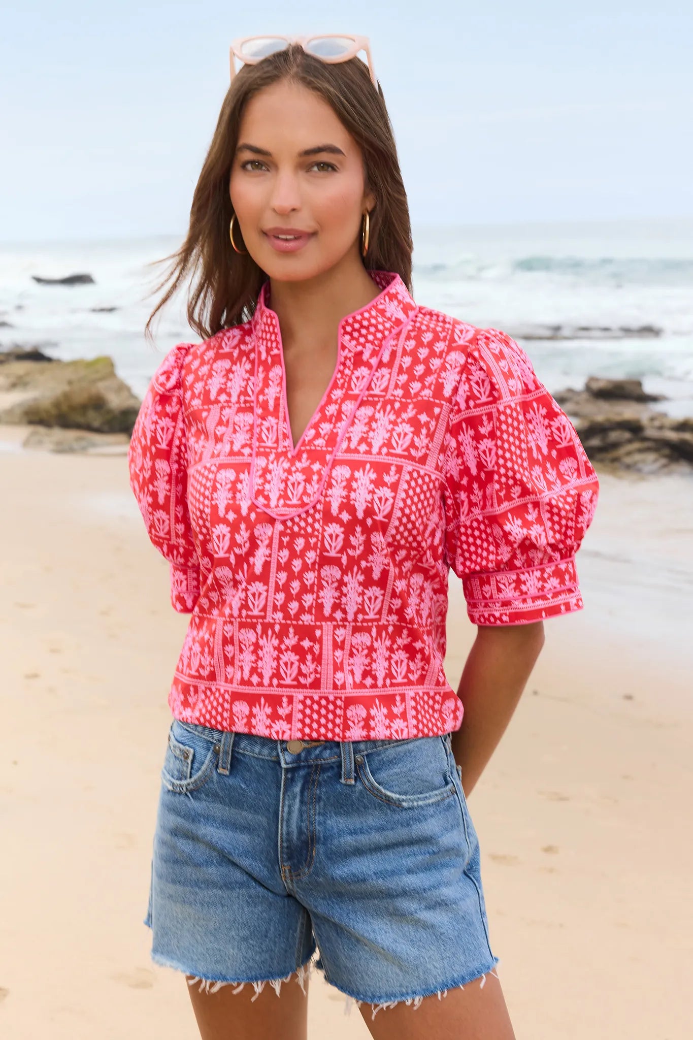 Woman wearing a red patterned blouse and denim shorts on a beach. mobile
