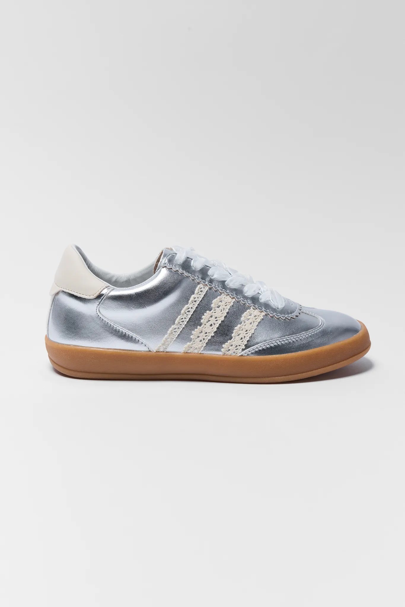 silver sneakers with lace details and ribbon with brown soles on white background