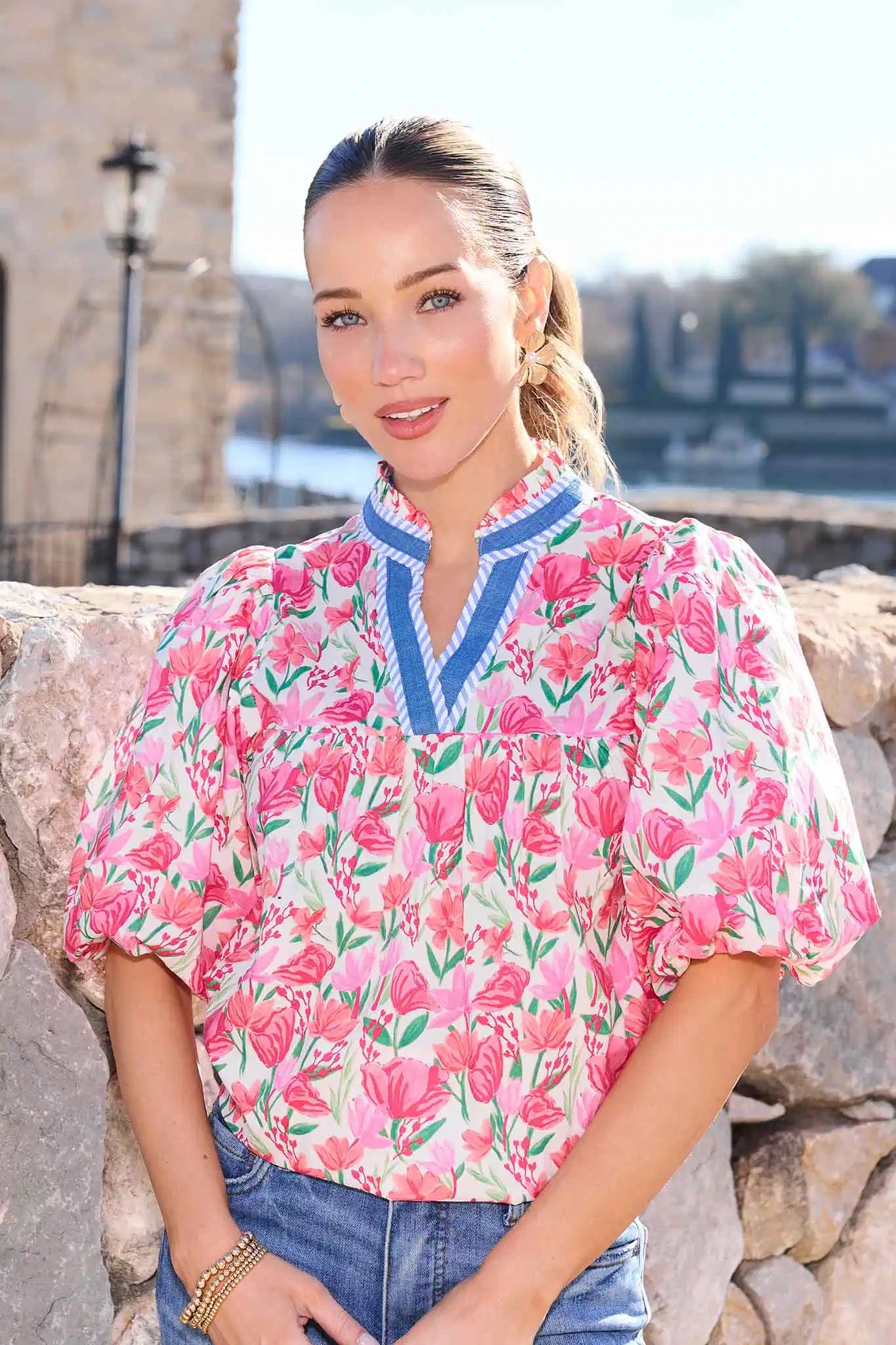 Woman wearing a pink floral blouse with a stone wall and blurred background