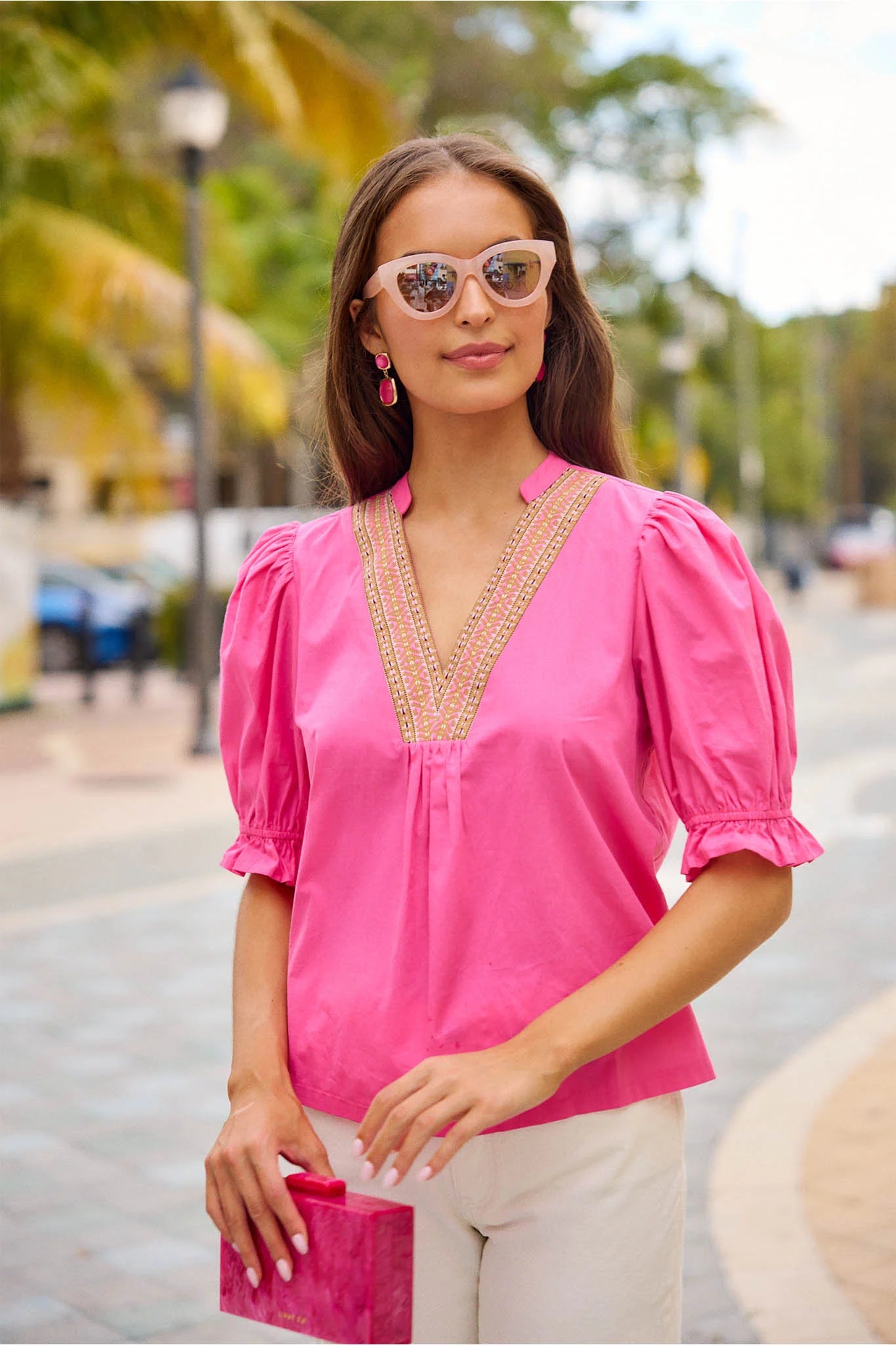 Woman wearing a pink blouse with intricate detailing in an outdoor setting