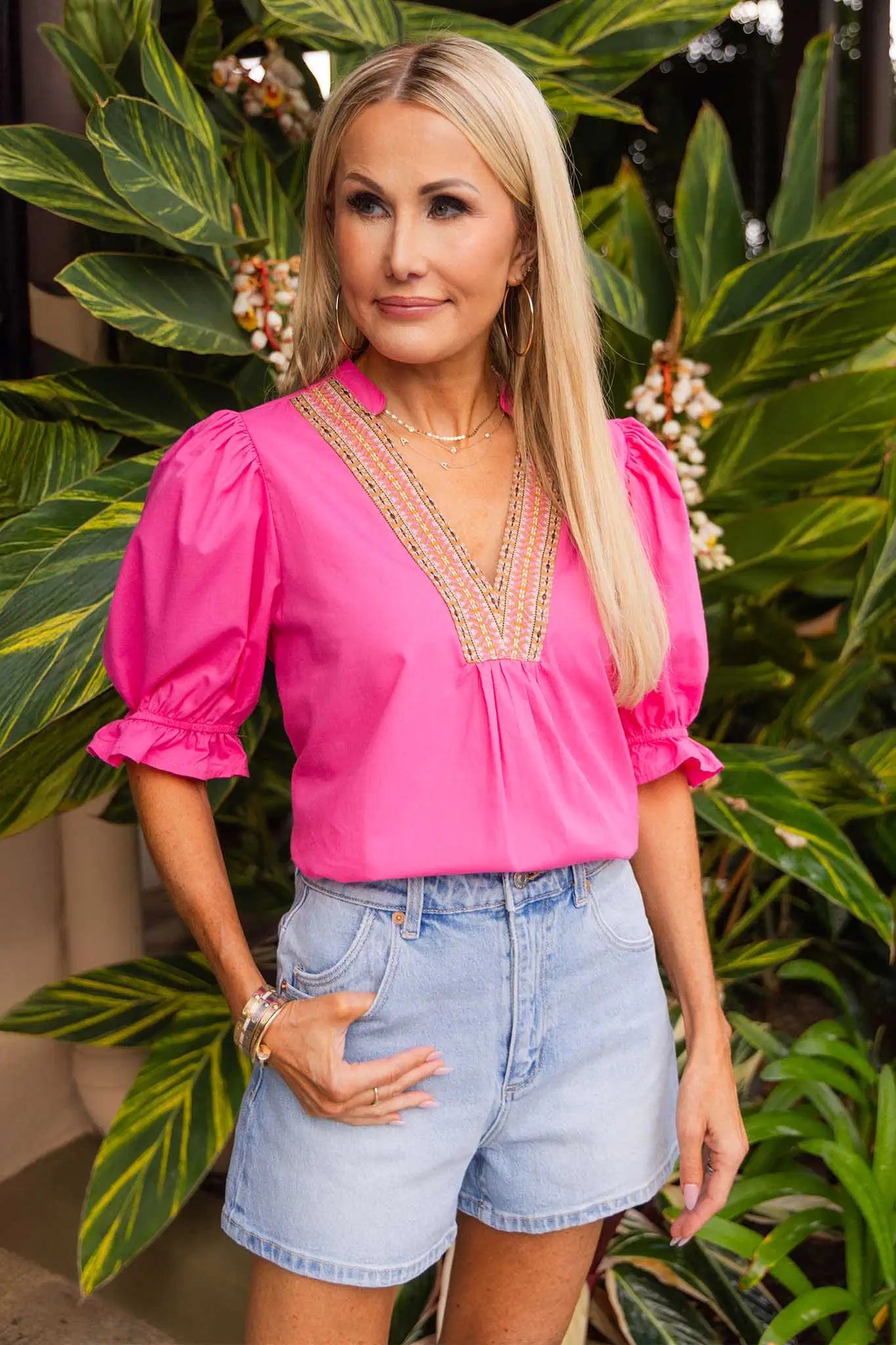 women wearing pink top and jean shorts with plants behind her