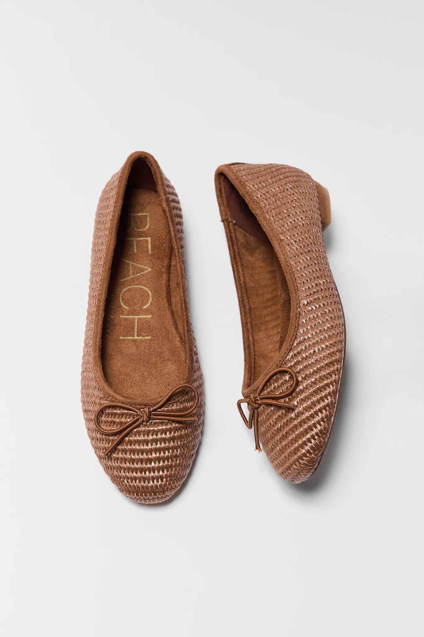 Pair of brown woven flats with a bow on a light gray background