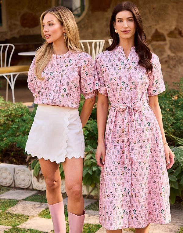 Two women wearing pink floral dresses standing outdoors.