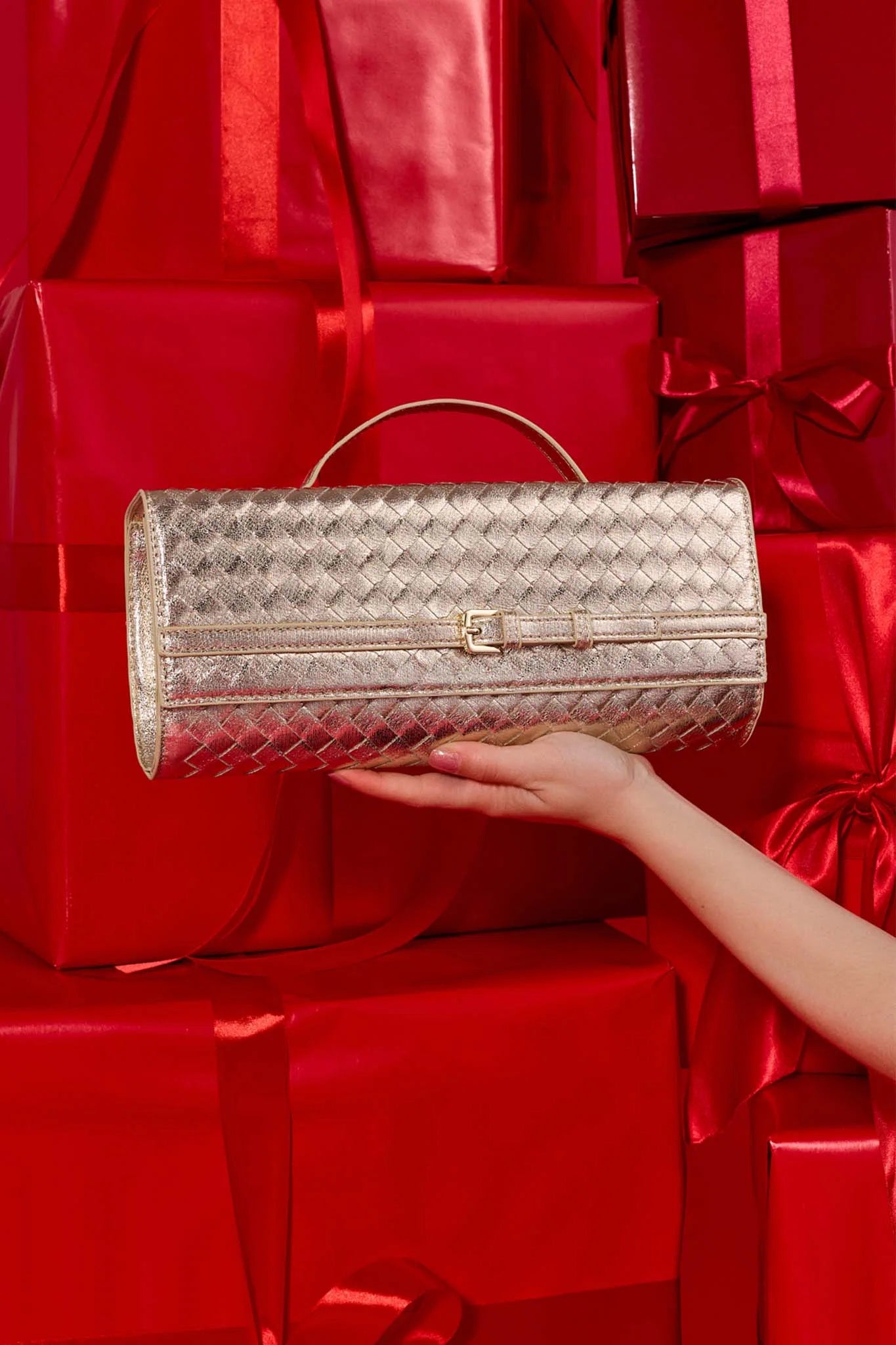 Emerson Gold Faux Leather Bag held by a hand against red gift boxes and ribbons