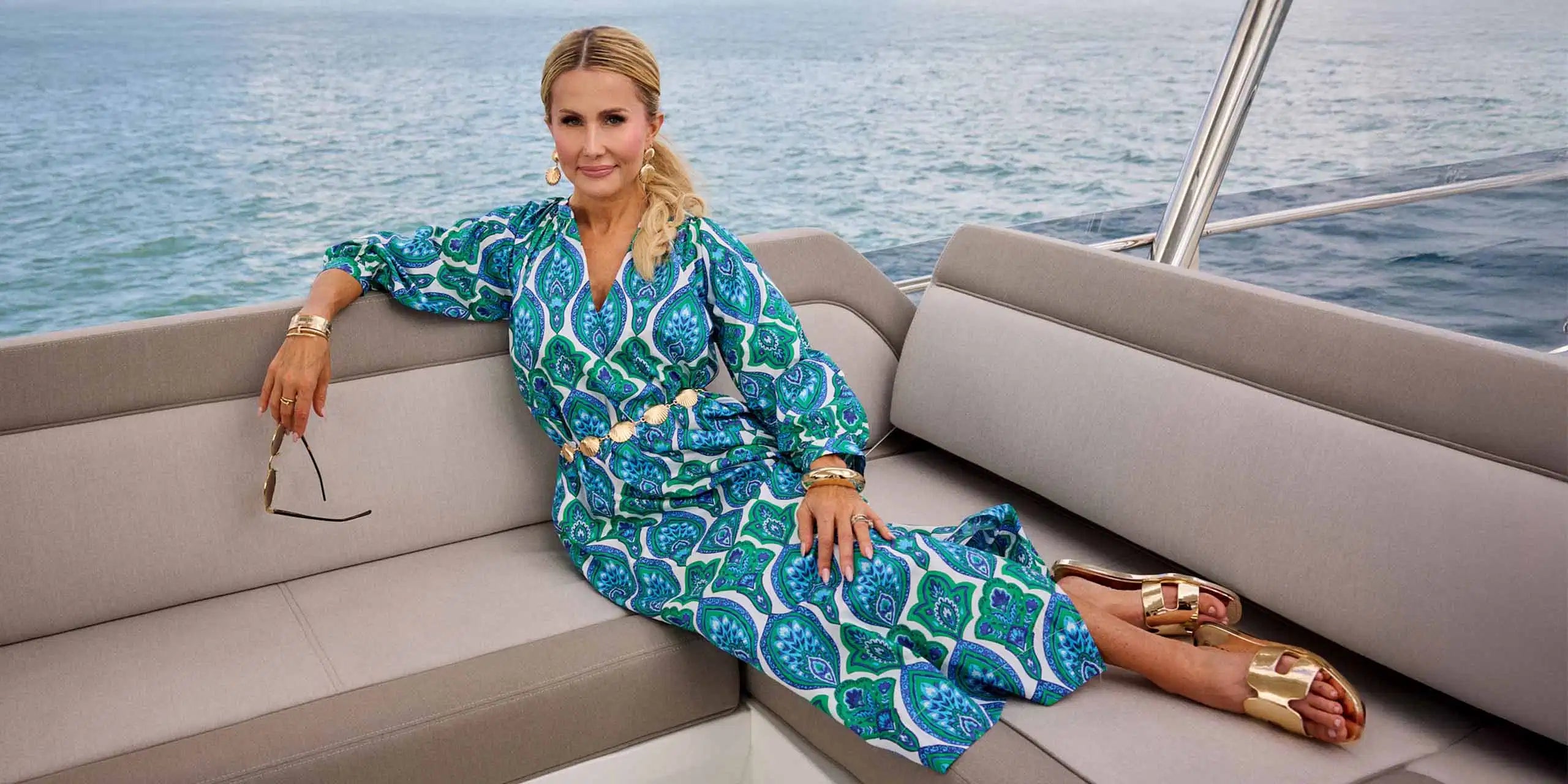 Woman in a blue patterned dress sitting on a boat with water in the background