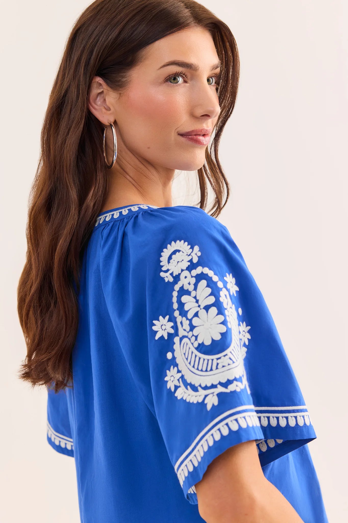 close up Woman wearing a blue top with white embroidery on a plain background